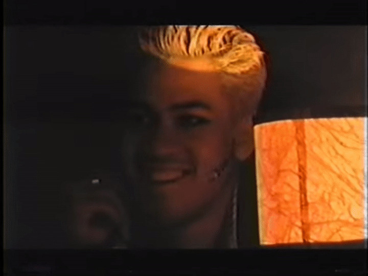 A late 90s boy smiles by the dim glow of a cheap paper nightclub lamp