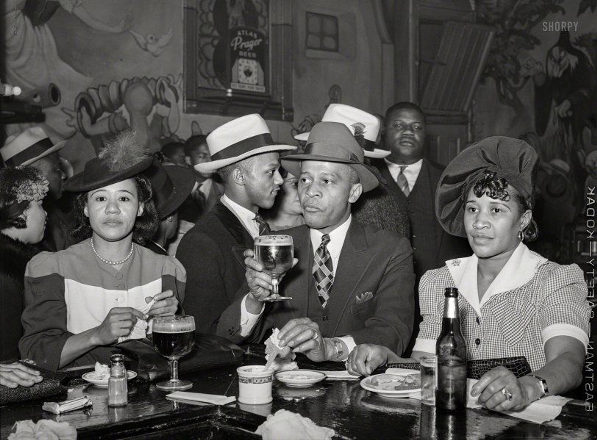 In this black & white photograph we see three people in the midst of eating a meal in a crowded tavern. 
     "South Side Chicago. Scene in Negro tavern." April 1941. Image digitized from a medium format negative by Russell Lee (American, 1903–1986) for the Farm Security Administration. https://www.shorpy.com/node/24136