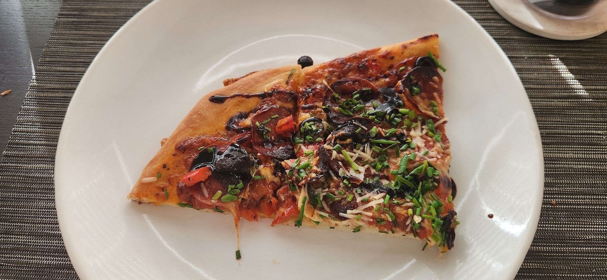 The chive-blasted pizza on a white plate with a thick glaze drizzled lightly over the chives