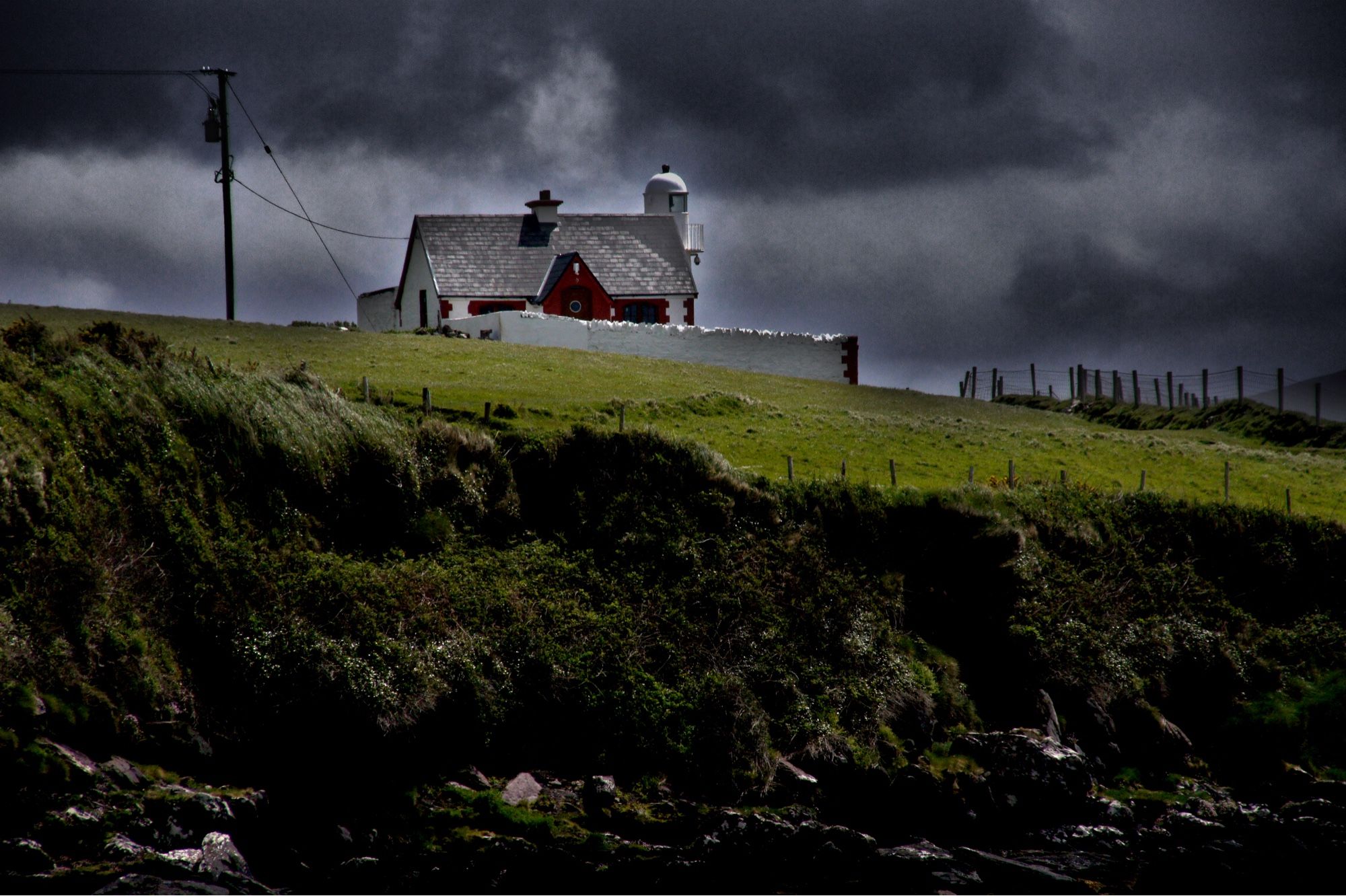 sturmwolken über wiese, haus und leuchtturm