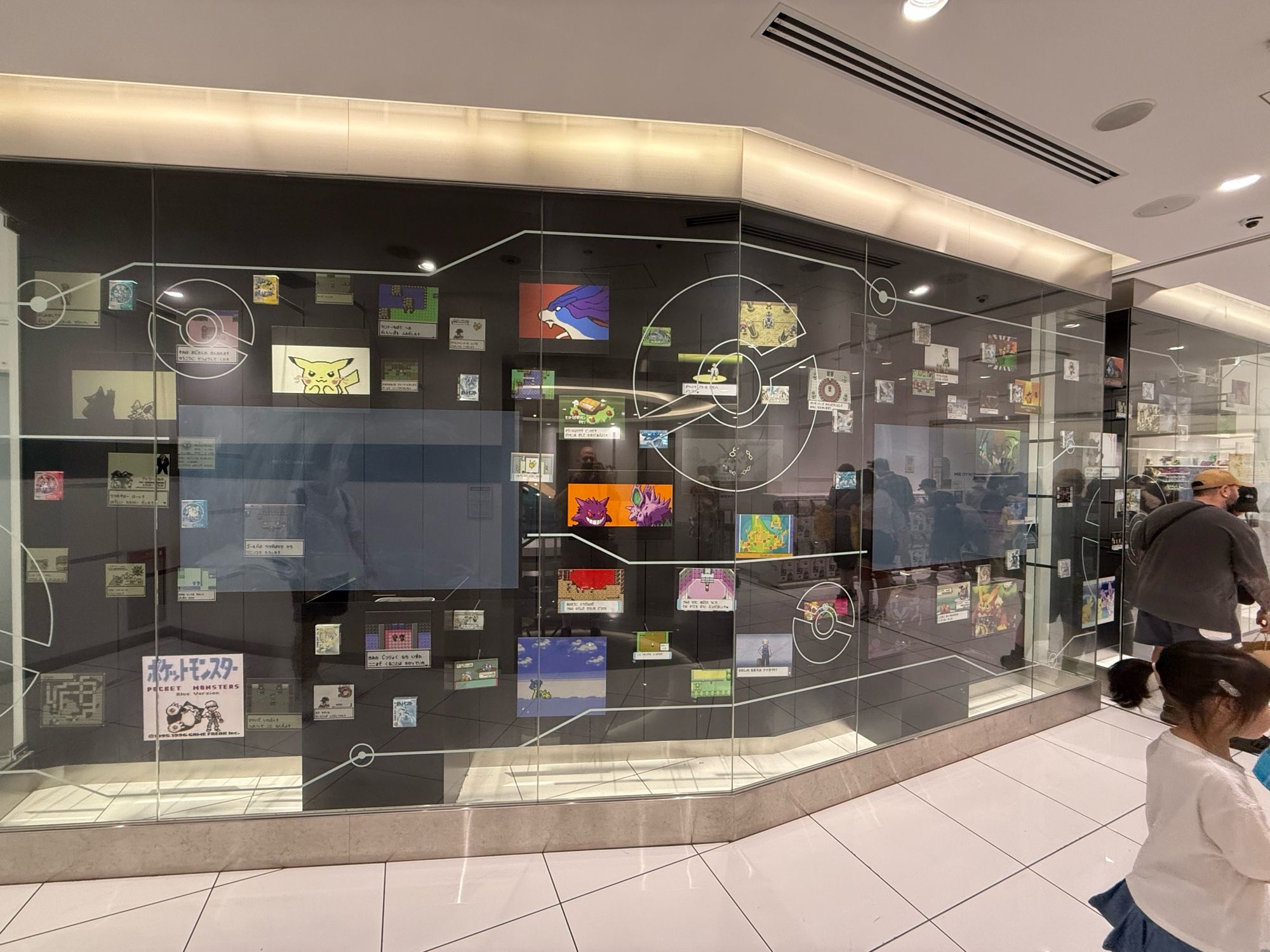 Photo of a display case, with various exhibits and screenshots from different Pokémon games going back to the 1990s