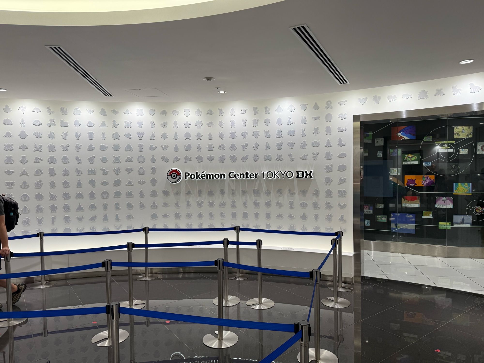 Photo of the entrance to the Pokémon Center. The wall is silhouettes of various Pokémon. The text reads "Pokémon Center Tokyo DX"