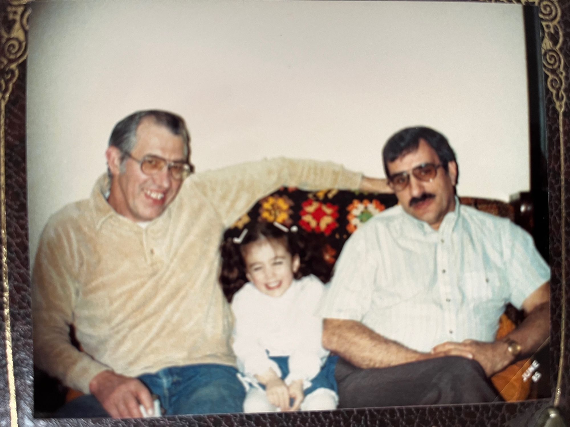 An old photograph. A young girl with curly brown hair sits between two middle aged men on a couch