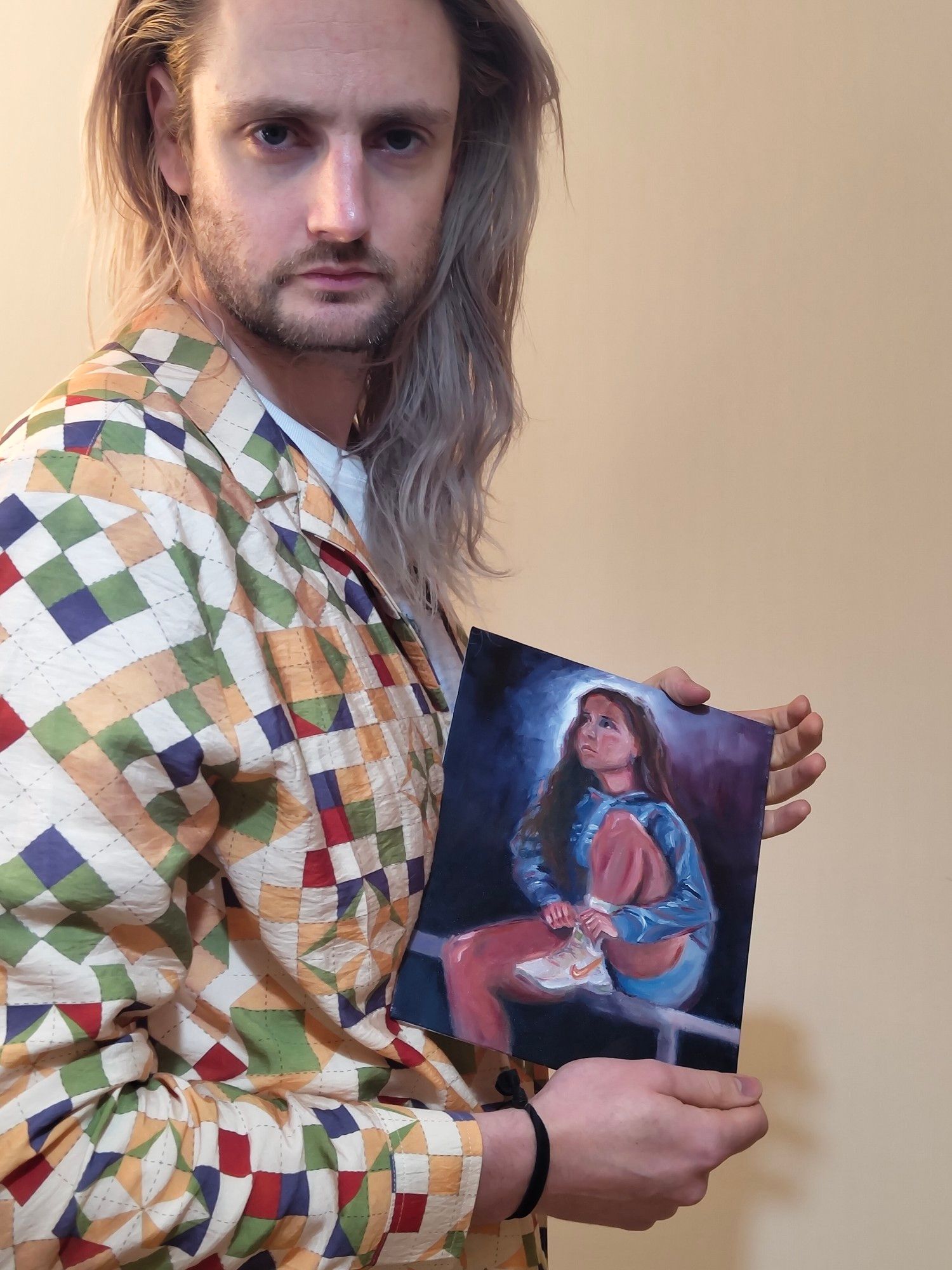 Photograph of the artist pulling a blue steel face, holding an oil painting of someone tying their shoe