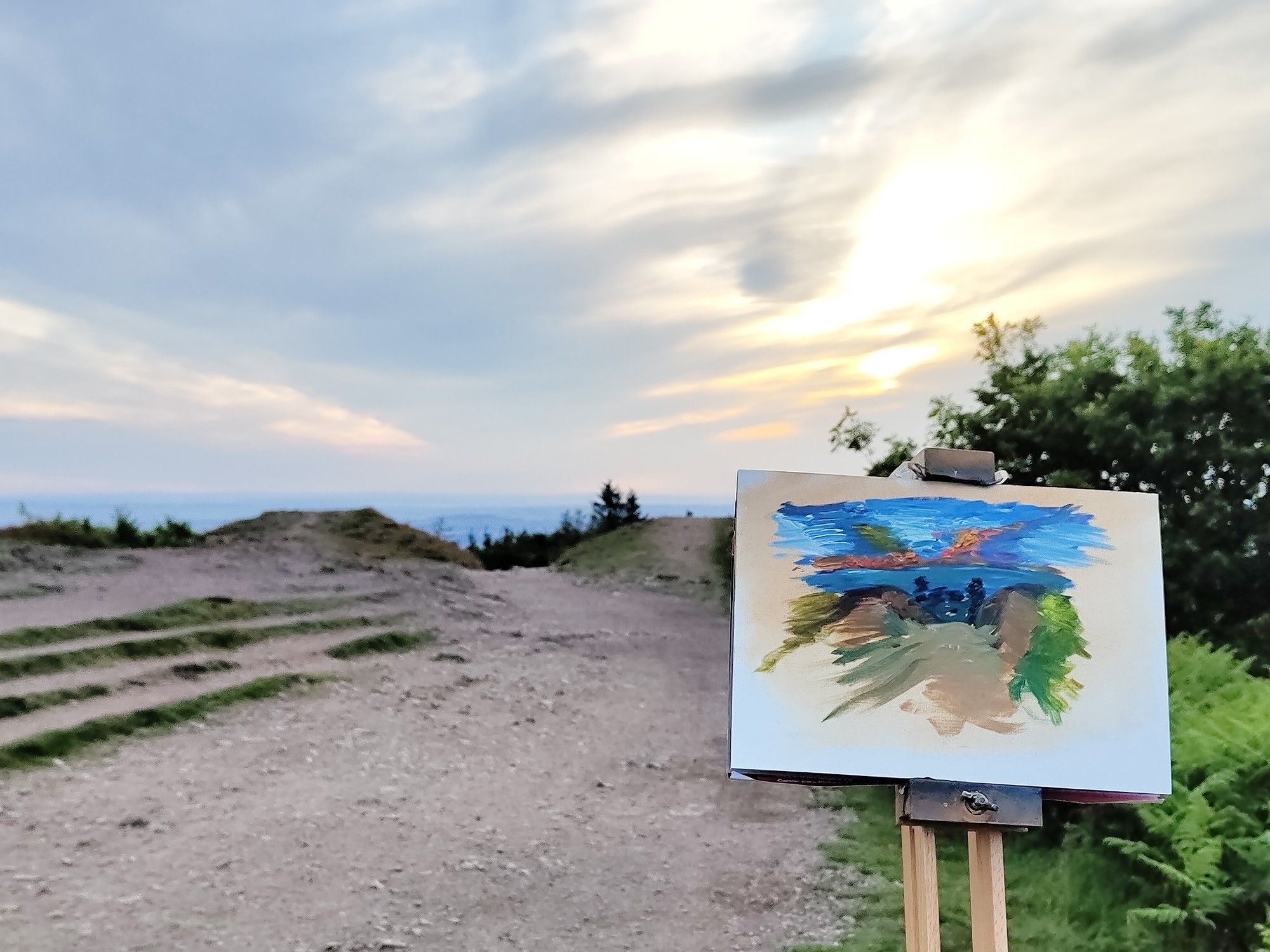 A sunrise behind the crest of a hill, with a painting of the scent in front of it