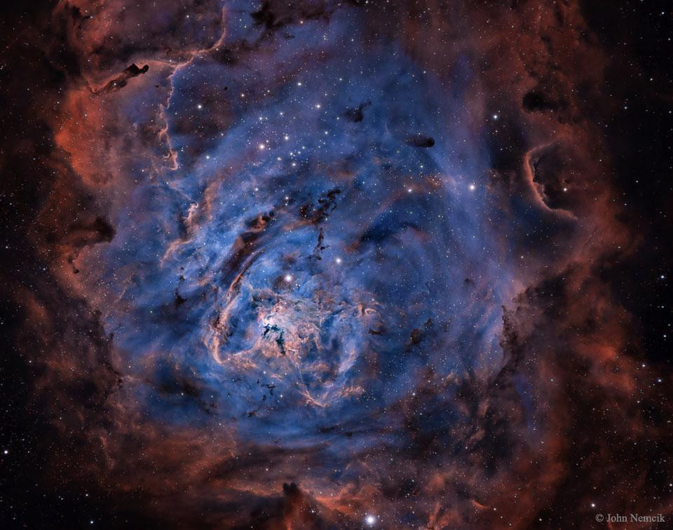 A vibrant, colorful panorama of the Lagoon Nebula (M8). This nebula is a hotbed of star formation, with many young stars visible within it. The nebula is located in the constellation Sagittarius, and can be seen with the naked eye. The image is enhanced to show the emissions of hydrogen (brown), sulfur (red), and oxygen (blue).