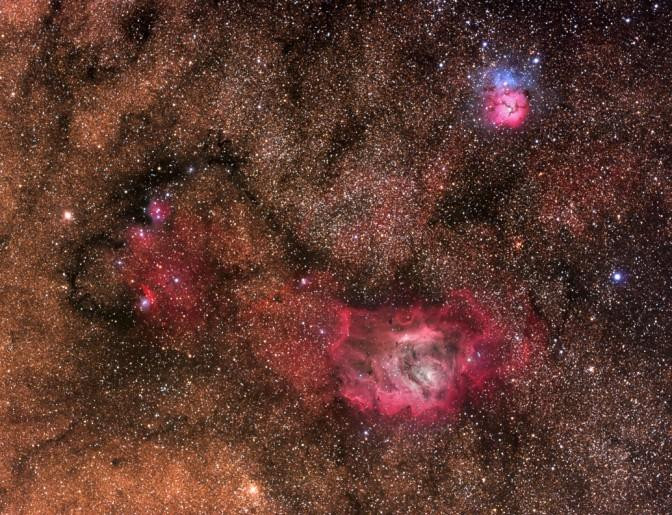 A stunning composite image showcasing three vibrant nebulae, M8 (the Lagoon Nebula), M20 (the Trifid Nebula), and NGC 6559, nestled within the star-studded expanse of the Milky Way galaxy.  These celestial nurseries, located about 5,000 light-years away, are painted in vivid hues of red and blue, a testament to the interplay of glowing hydrogen gas and reflected starlight. The image is a collaborative effort, combining data from multiple telescopes and cameras, highlighting the grandeur and intricate beauty of the cosmos.