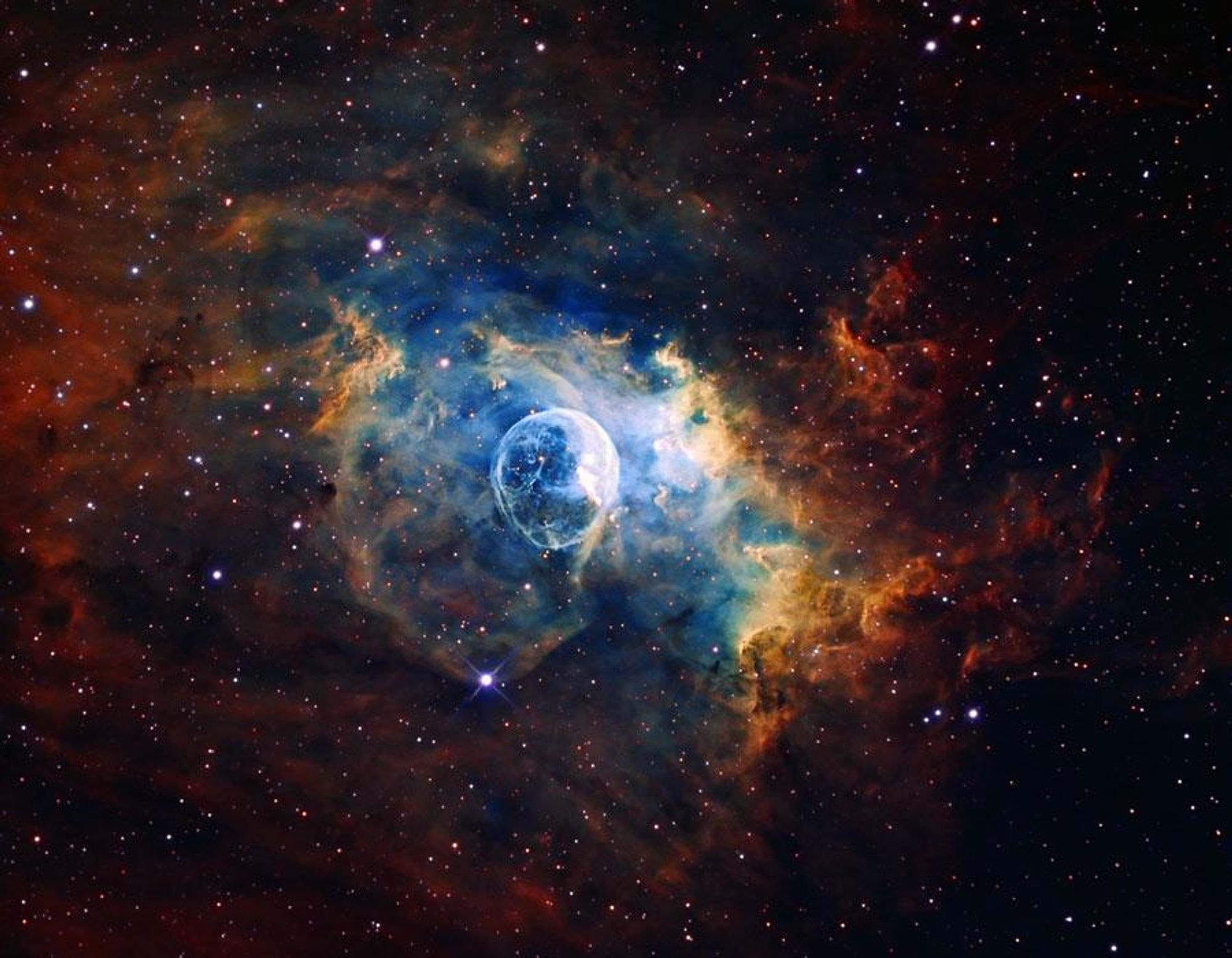 A stunning image of NGC 7635, the Bubble Nebula, in scientifically mapped colors to highlight its details. The nebula is being pushed out by the stellar wind of a massive central star, BD+602522. Next door lives a giant molecular cloud that gets blasted by the hot radiation from the bubble's central star, causing it to glow. The image showcases a vibrant clash of colors between the blue bubble and the red and orange hues of the molecular cloud, creating a visually striking display of cosmic forces at work.