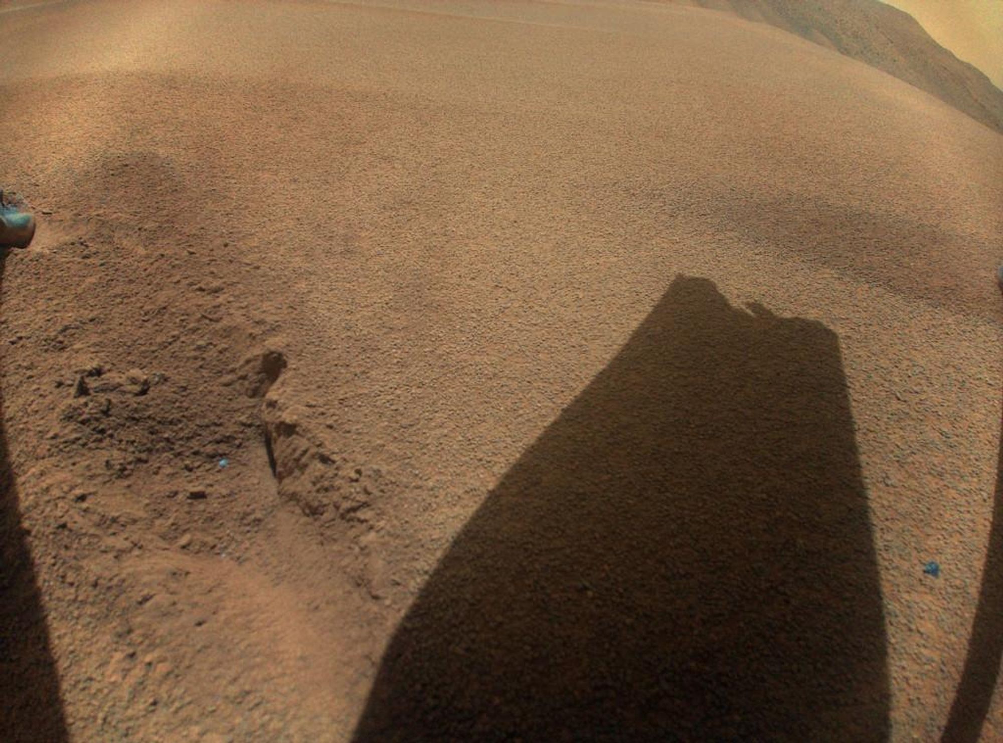 A close-up image of the Martian surface taken by the Ingenuity Mars helicopter, showing the shadow of one of its rotor blades likely damaged during landing. This image was captured after Ingenuity lost contact with the Perseverance rover about 1 meter above the surface. This rough landing marked the end of Ingenuity's flight operations after over 1,000 days of exploring Mars.