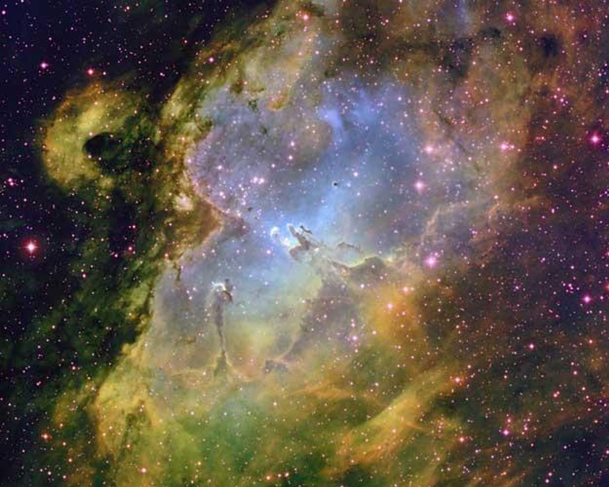 A vibrant, multi-colored image of the Eagle Nebula, M16, revealing a star-forming region within a larger dark shell of dust. The bright center, illuminated by young blue stars, shows tall pillars and globules of gas and dust where new stars are forming. This image was taken with the 0.9-meter telescope on Kitt Peak, Arizona, USA.