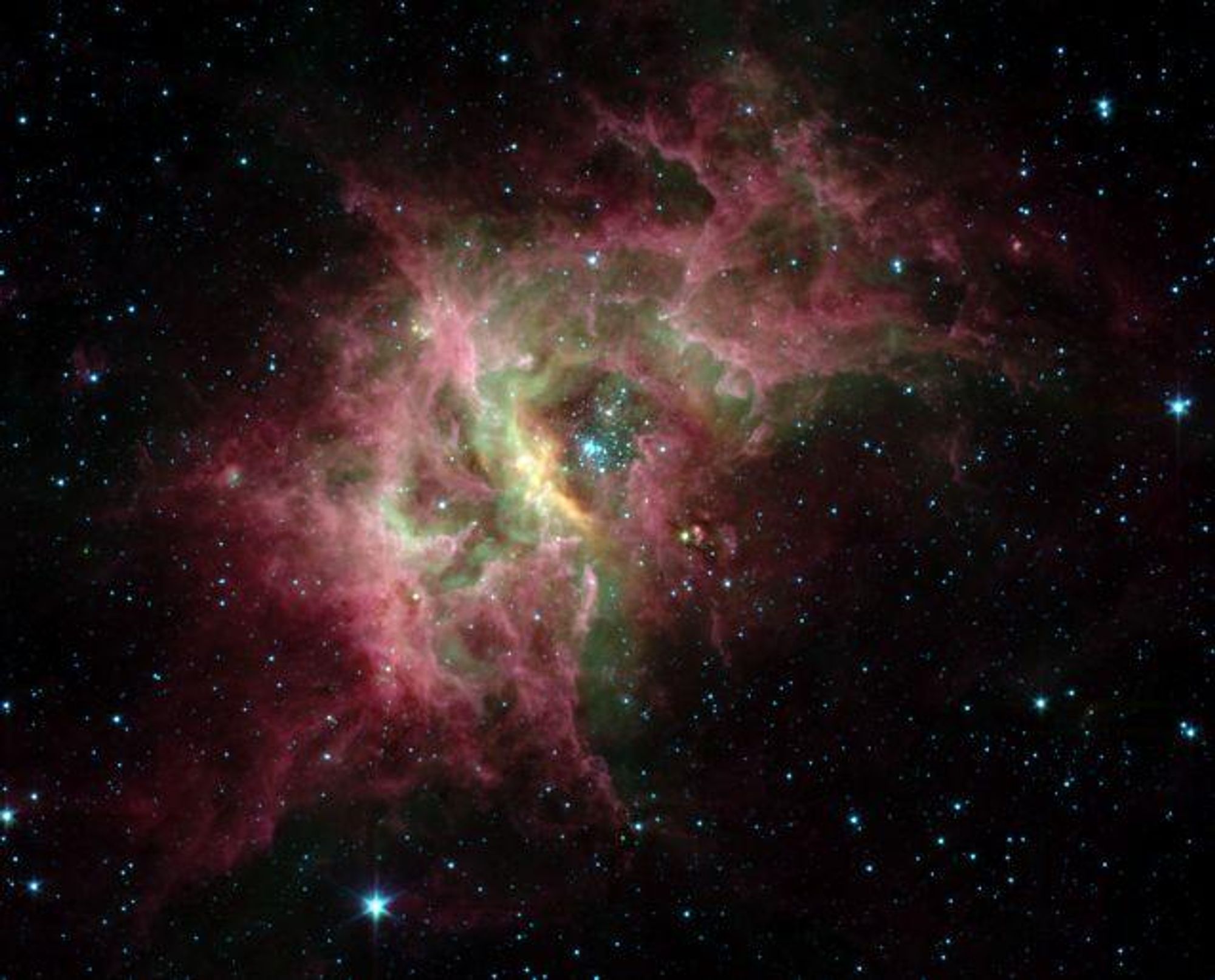 A false-color infrared image of the nebula RCW 49, taken by the Spitzer Space Telescope. The image shows a large cloud of gas and dust, with a cluster of hot stars at the center. The nebula is a star-forming region, and the image reveals over 300 newborn stars scattered throughout the dust clouds and filaments. Some of these stars are surrounded by protoplanetary discs, suggesting that planet formation is a common occurrence in star-forming regions.