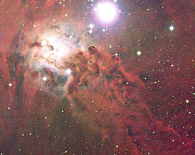 A stunning image of the nebula surrounding bright star S Mon, part of the young open star cluster NGC 2264. The nebula is filled with dark dust and glowing gas, with a bright blue glow around S Mon from reflected light and a diffuse red glow from emission. The region just below S Mon is nicknamed the Fox Fur Nebula for its color and texture. The intricate shapes are created by interstellar dust interacting with light and gas from young stars.