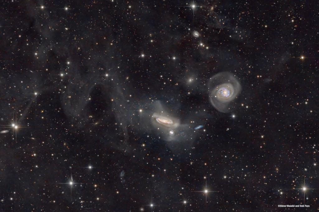 A deep space image of the NGC 7771 galaxy group, located 200 million light-years away in the constellation Pegasus. The image reveals a large edge-on spiral galaxy (NGC 7771) near the center, with two smaller galaxies below it. A large spiral galaxy (NGC 7769) is seen face-on to the right.  The galaxies are interacting, causing distortions in their shapes and faint streams of stars created by their mutual gravitational tides.  The faint, dusty galactic cirrus clouds known as Integrated Flux Nebulae (IFN) are also visible in the image. The IFN reflect starlight from our own Milky Way Galaxy and lie only a few hundred light-years above the galactic plane.