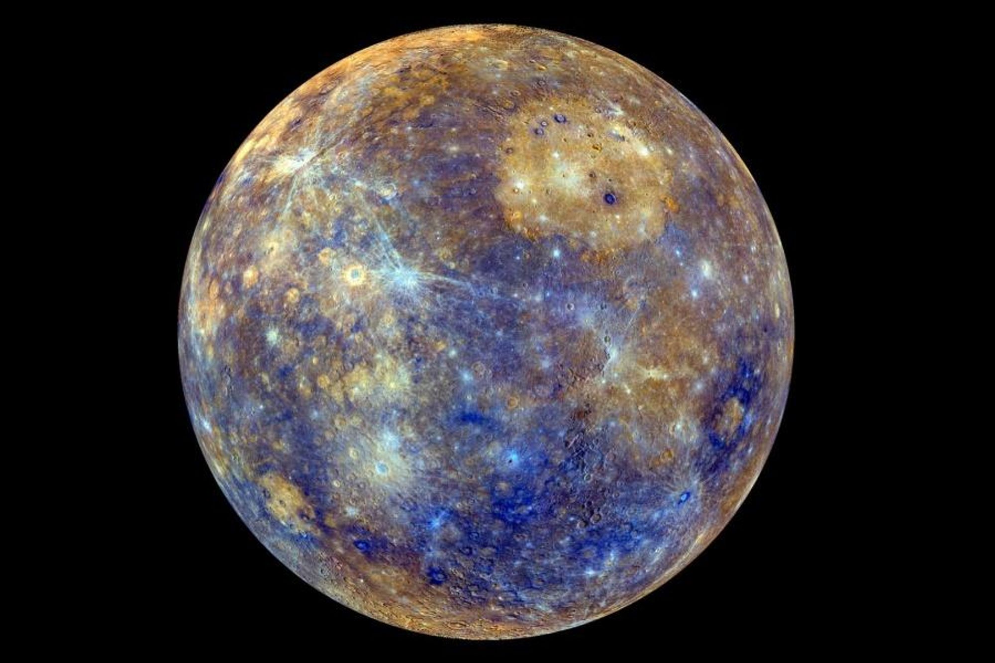 Color-enhanced image of Mercury, showing the planet's diverse surface features. The Caloris basin, a large, tan-colored impact feature, is visible at the upper right. Young crater rays, light blue and white in color, extend across the darker blue terrain.