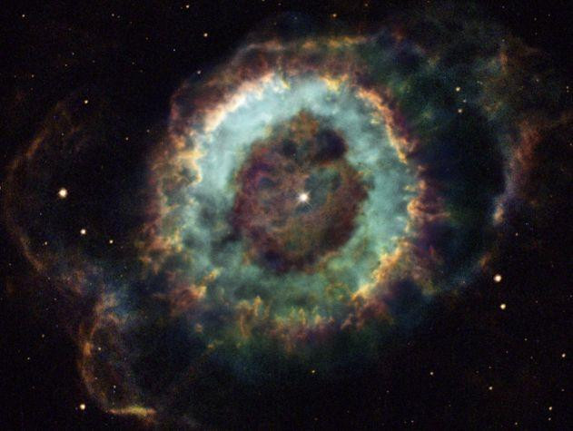 A colorful image of the Little Ghost Nebula, also known as NGC 6369. The nebula is a planetary nebula, created from the outer layers of a dying star. This image from the Hubble Space Telescope shows the intricate details of the nebula, including the glowing ring of gas, and the white dwarf star at its center. The nebula is about 2,000 light-years away in the constellation Ophiucus.