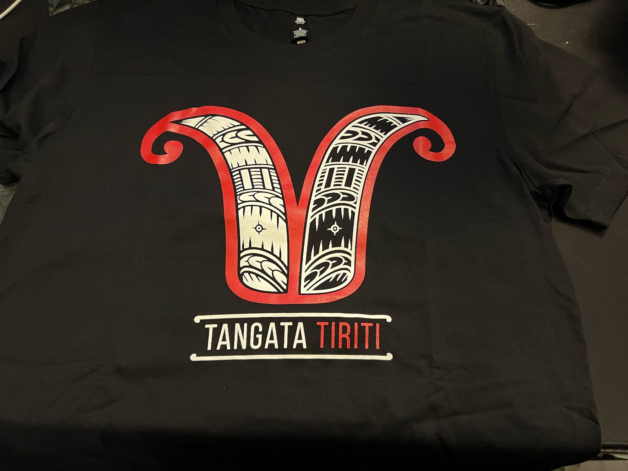 Image shows a Tangata Tiriti tee-shirt with its especially designed emblem - one side for Pākehā and the other for Tauiwi