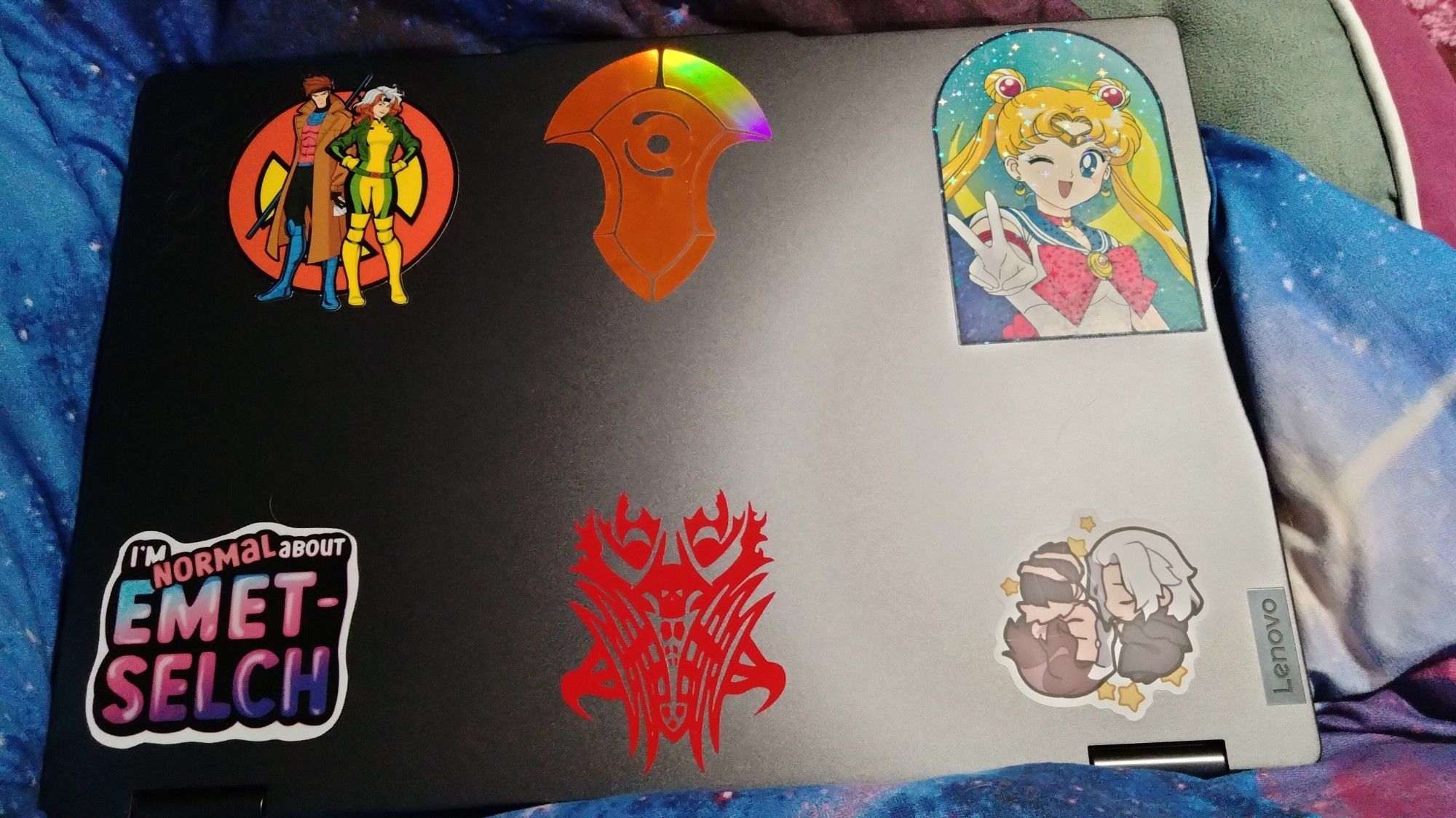 Six stickers on laptop; X-Men '97 Gambit and Rogue, Azem crystal, Sailor Moon doing a peace sign/winking, Emet-Selch (Hades and Solus), Emet-Selch's glyph, "I'm normal about Emet-Selch".