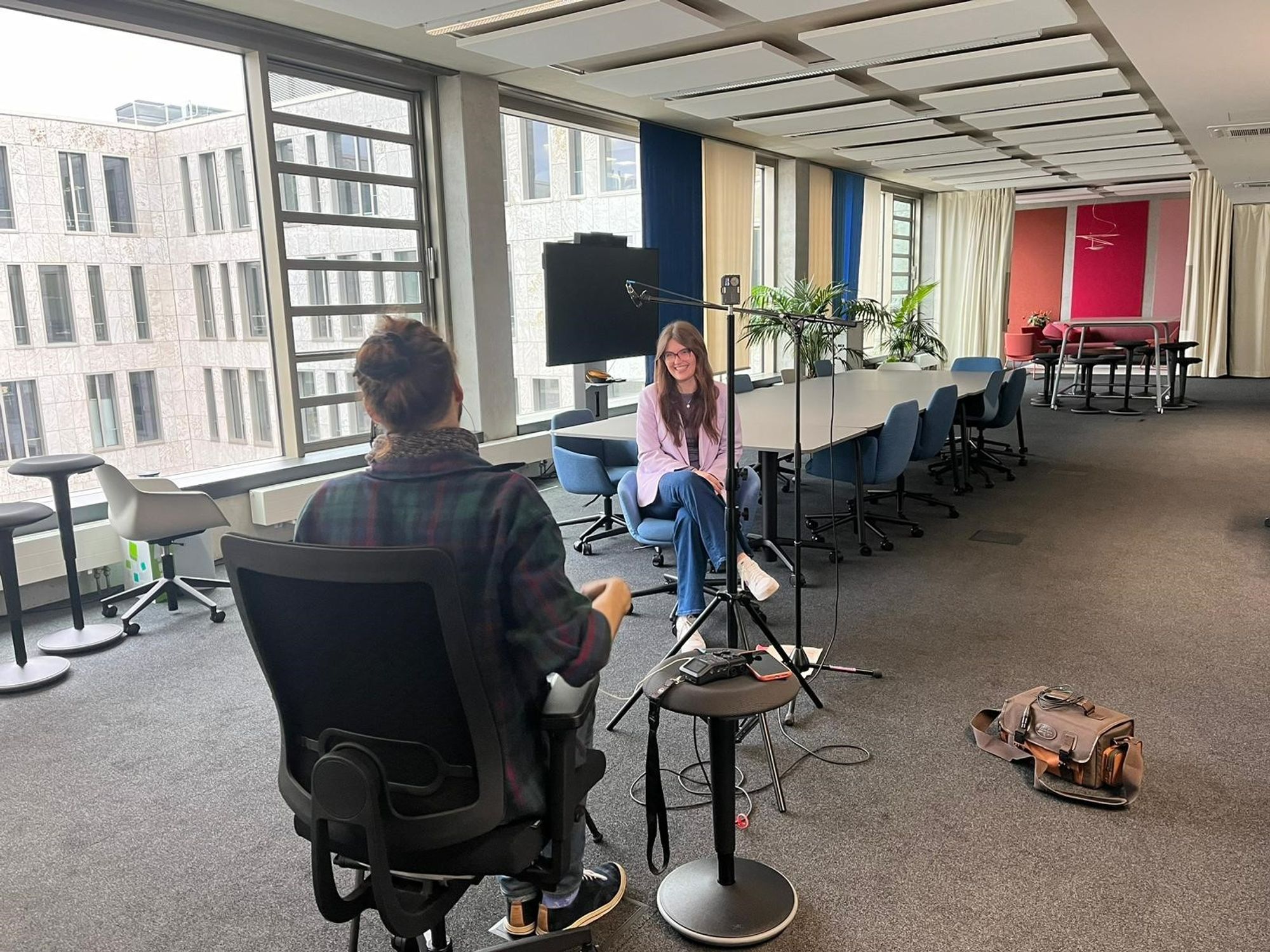 Eine DATEV-Mitarbeiterin sitzt in einem Büroraum vor einem Konferenztisch. Sie wird von einer weiteren Person, die ihr gegenübersitzt, zum Thema kaufmännische Ausbildung bei interviewt.