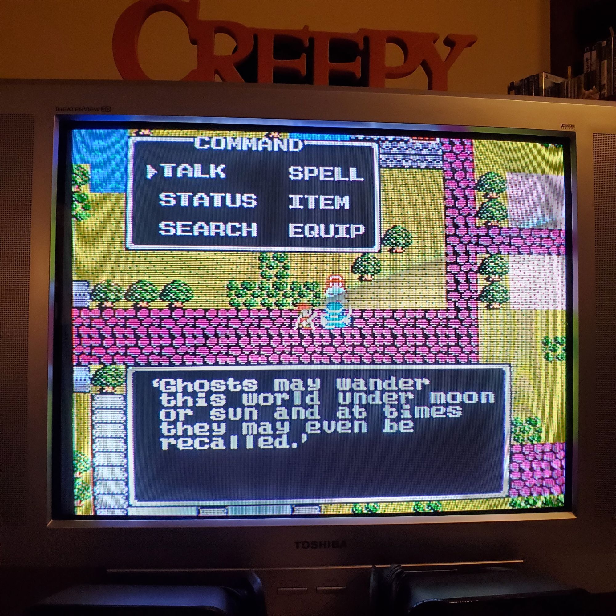 A CRT with an old NES RPG, Dragon Warrior II, and a villager's text box saying "Ghosts may wander this world under moon or sun and at times they may even be recalled."