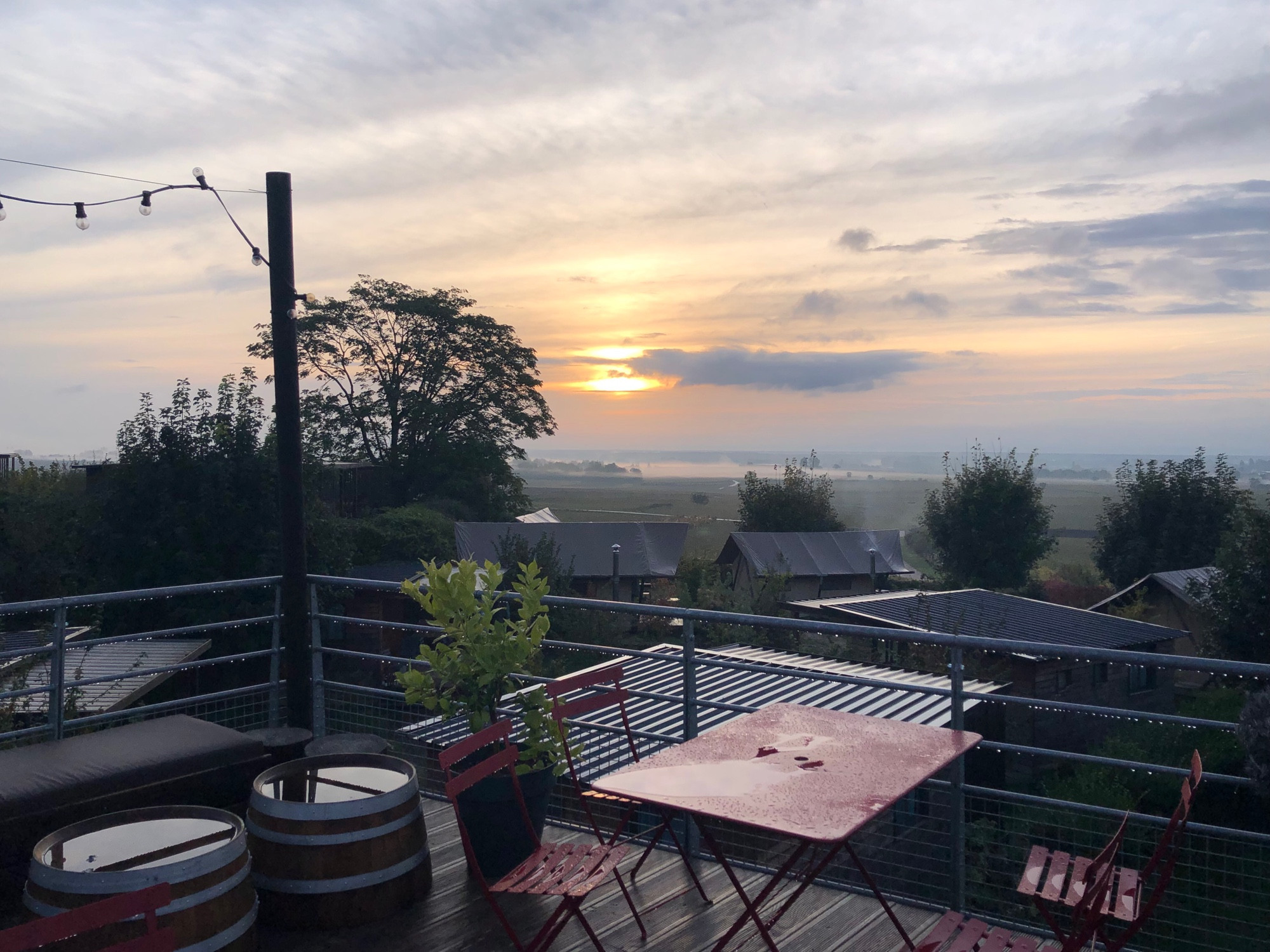 Sonnenaufgang in Meursalt. Im Vordergrund eine Terrasse. Regennasse Tische und Stühle.