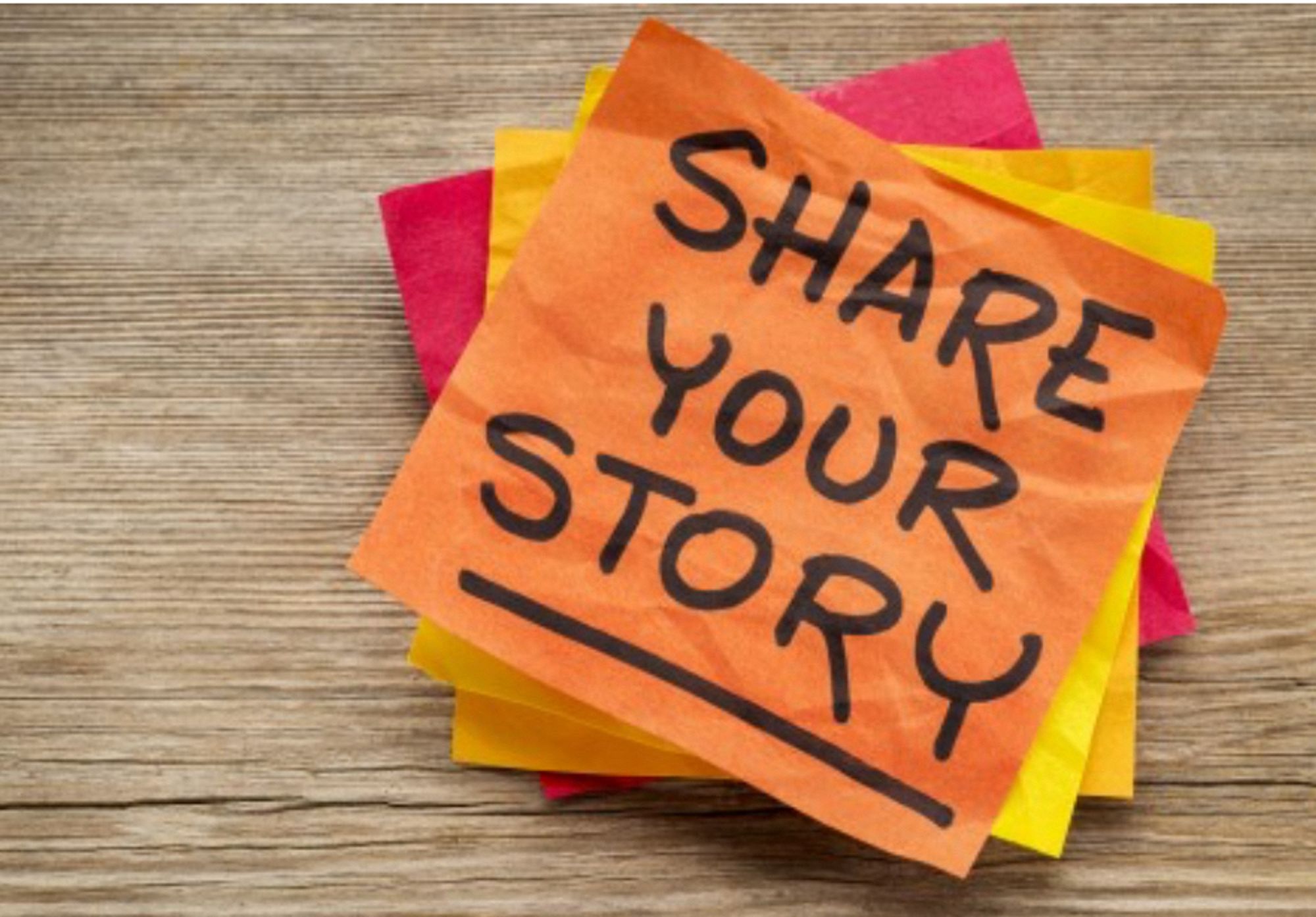 A pile of coloured post it notes on a wooden table

The top orange one
A little crumpled
Has 
“SHARE YOUR STORY” written on it 
Underlined 

#doit