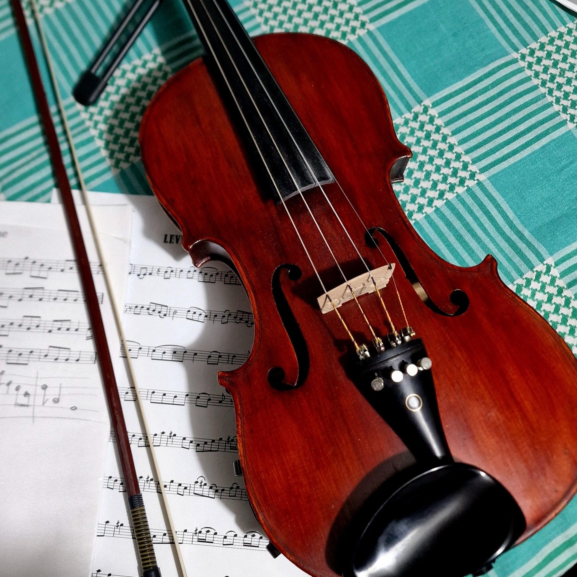 Image shows a violin and bow on a green tablecloth with some sheet music.