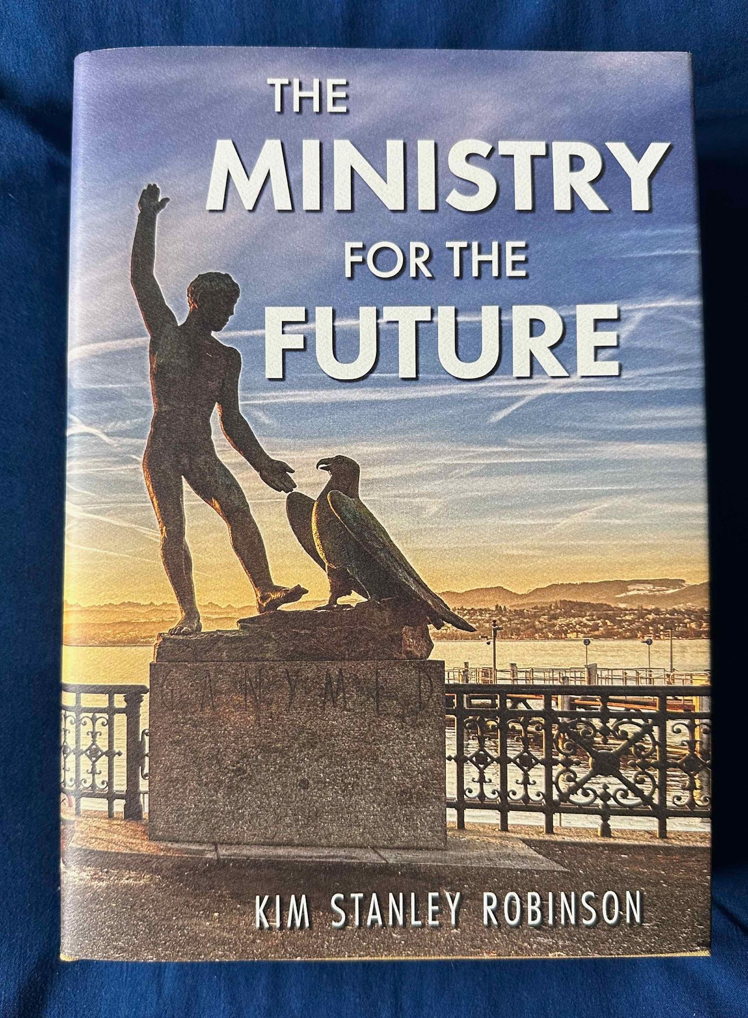 Cover jacket illustration shows a sculpture of a man and a raptor.  The staue is on a plinth in front of a lake.

Text:
THE MINISTRY
FOR THE
FUTURE


KIM STANLEY ROBINSN