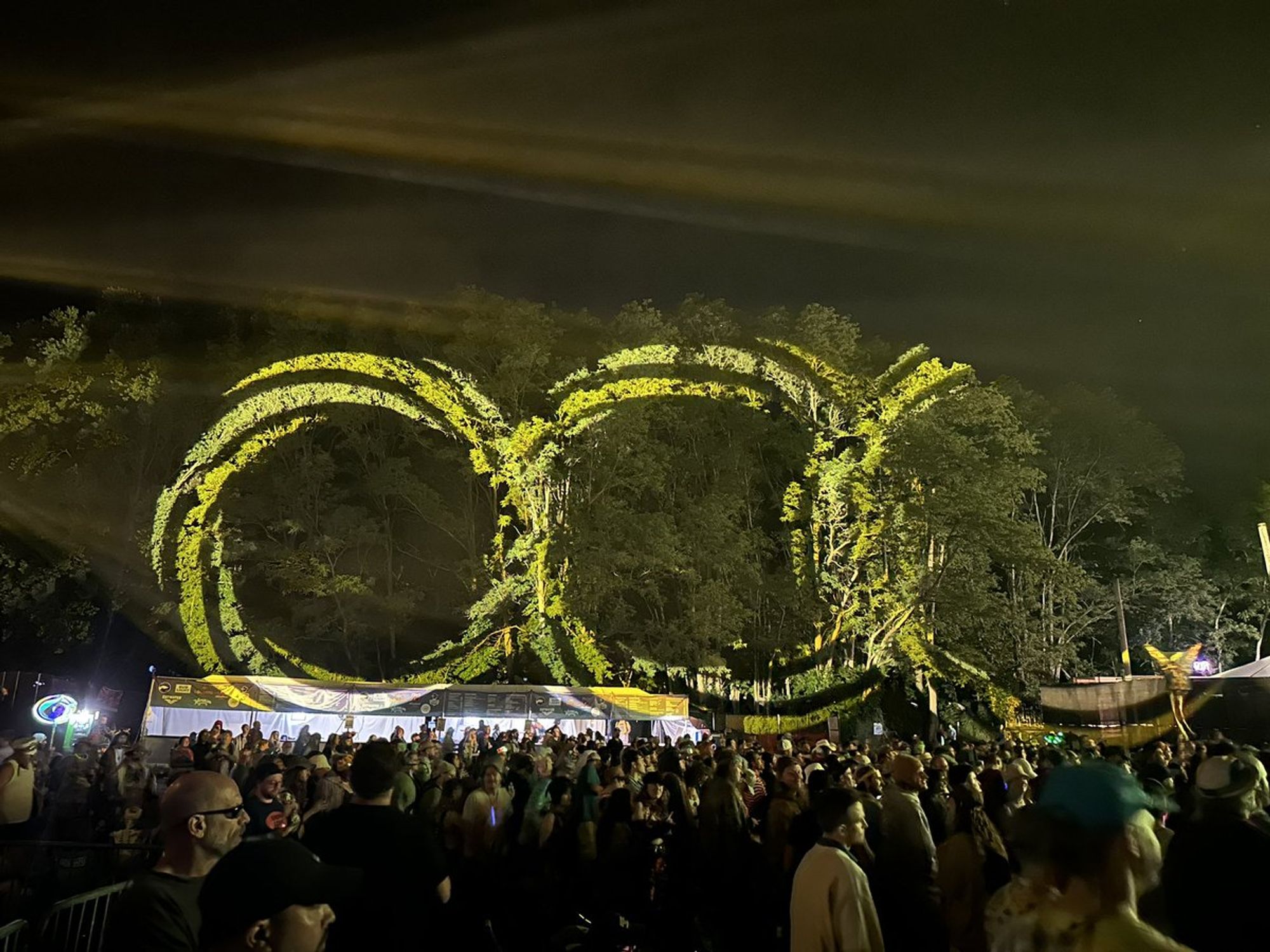 Yellow interlocking rings painted by the lights on the woods to the left of the stage, which isn't seen.  The crowd, facing right, is in the foreground.