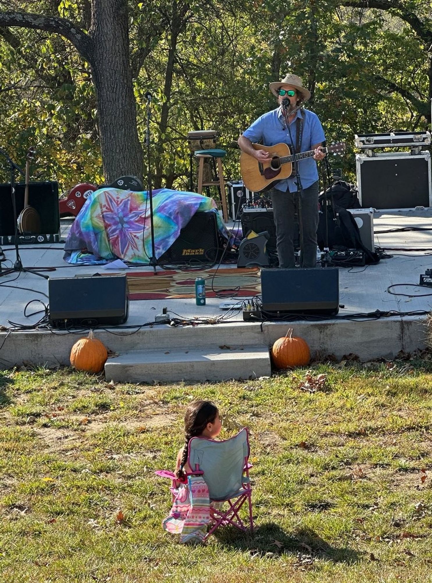 A small child sitting in a small pink lawn chair right in front of the stage.  A man playing guitar and singing is on the stage.