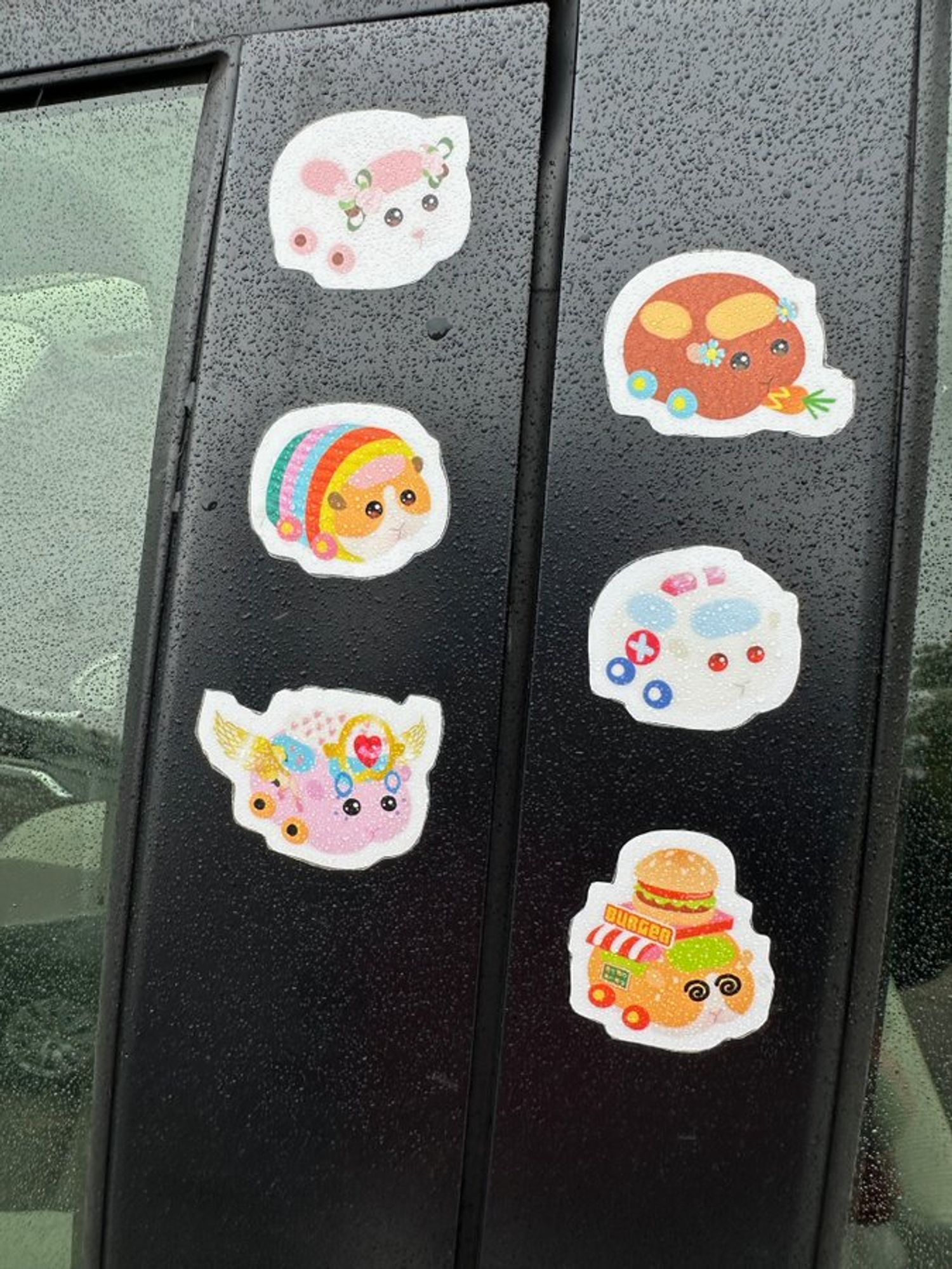 Close up of the six stickers on the driver side doorframe: various guinea pigs as automobiles.