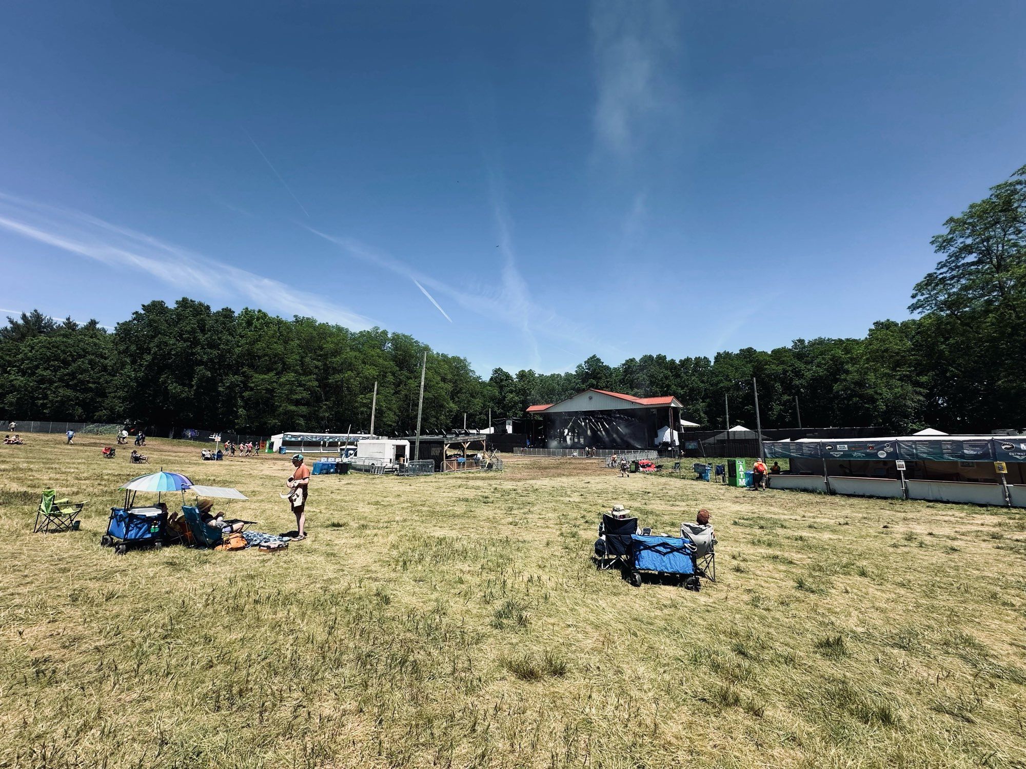 Long shot of the Moonshine Stage. A few groups have set up their spots. The stage is backed by woods.