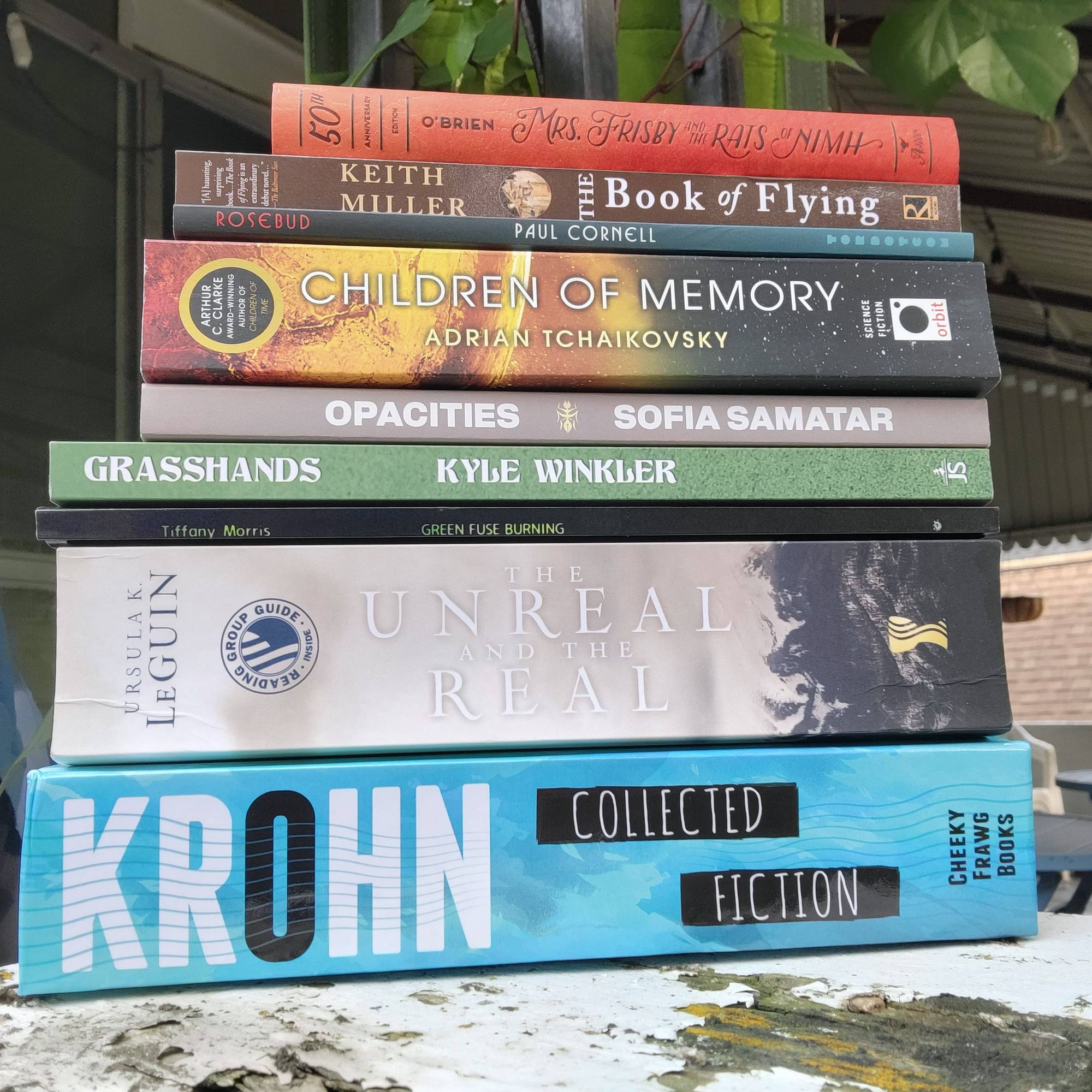 Stack of books: Mrs. Frisby & the Rats of Nimh, The Book of Flying, Rosebud, Opacities, Grasshands, Green Fuse Burning, The Unreal and the Real, Krohn: Collected Fiction