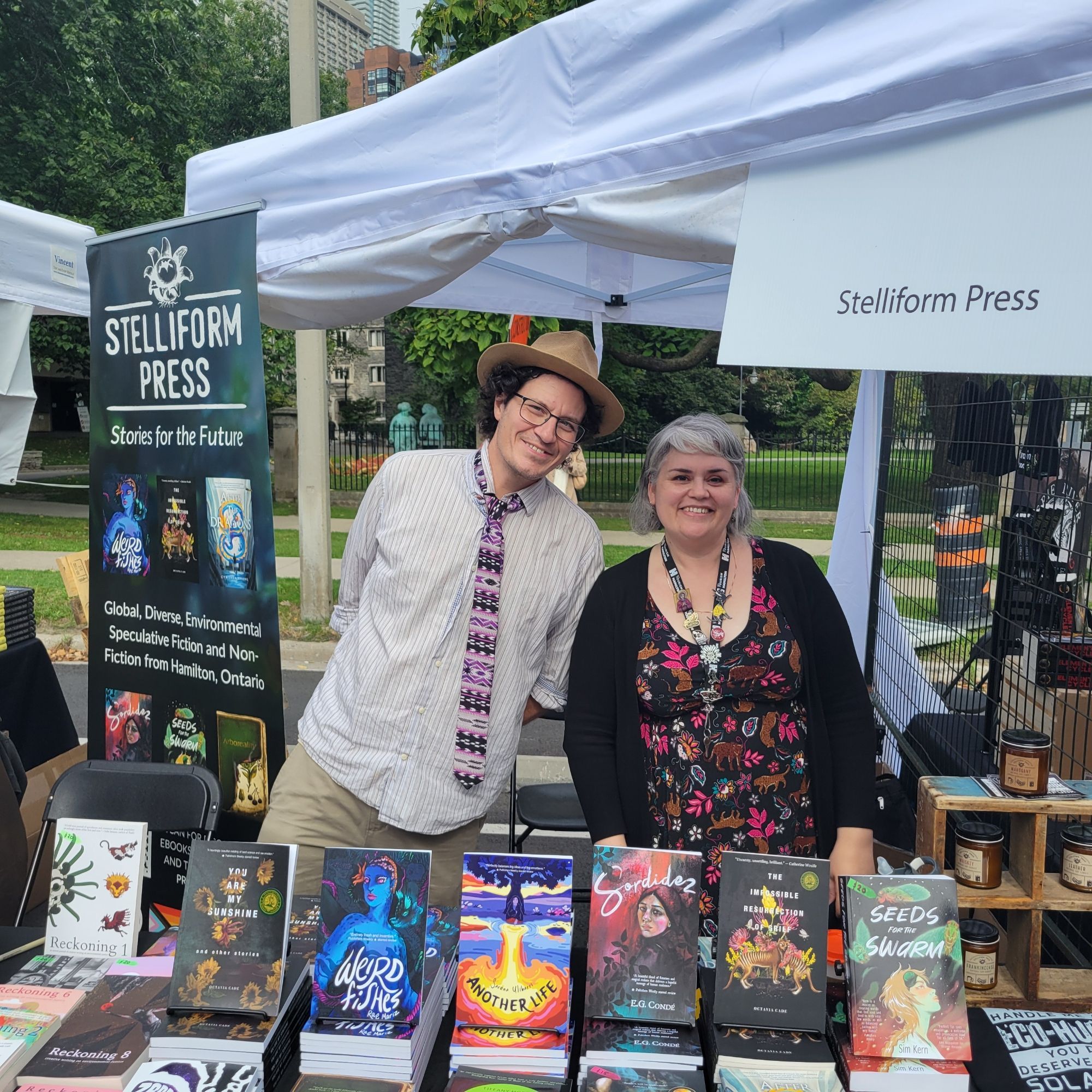 Michael J. DeLuca & Selena Middleton at a stand at an outdoor book festival, with lots of books