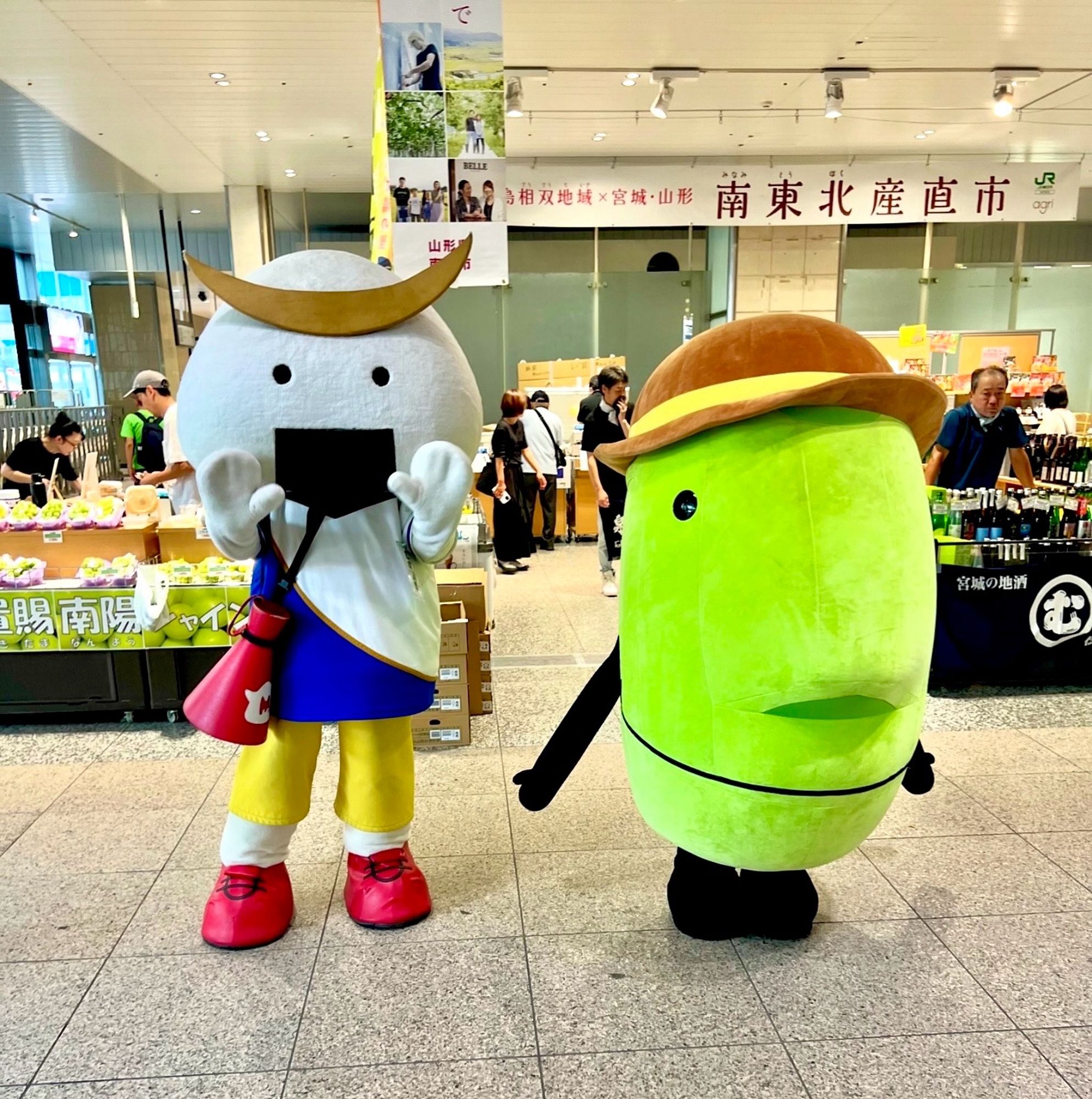 A samurai whose head is a rice ball, wearing contemporary sporting attire, stands beside a green mascot in the shape of Yamagata Prefecture, with a big brown hat.