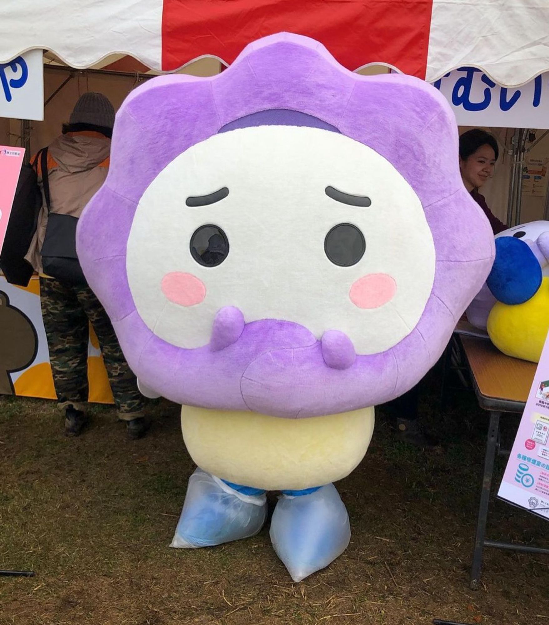 A mascot whose face is etched with concern has a purple cloud of smoke around its head, a cloud which is also his arms. His hands are covering his mouth.