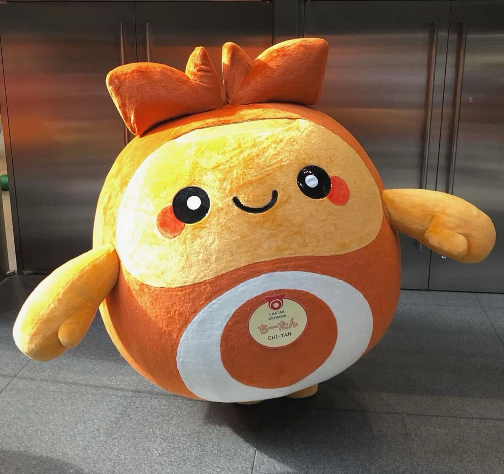 A round orange mascot stands smiling, with arms outspread.