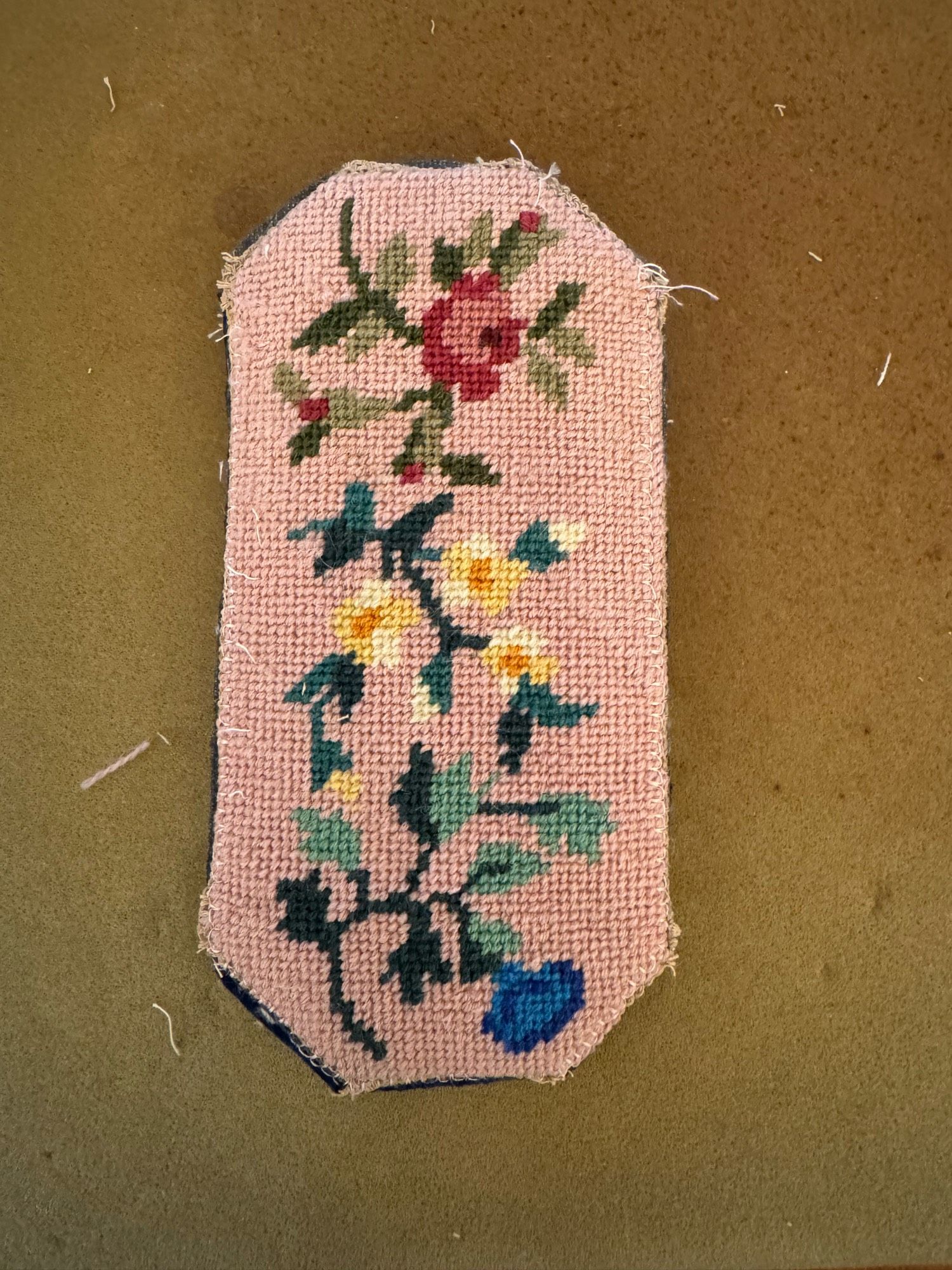 One side of a pink floral needlepointed glasses case on a beige background.