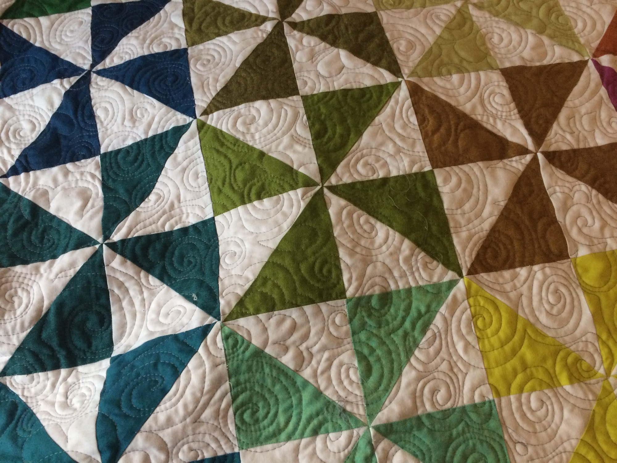 Pinwheel quilt in solids with swirled quilting design.