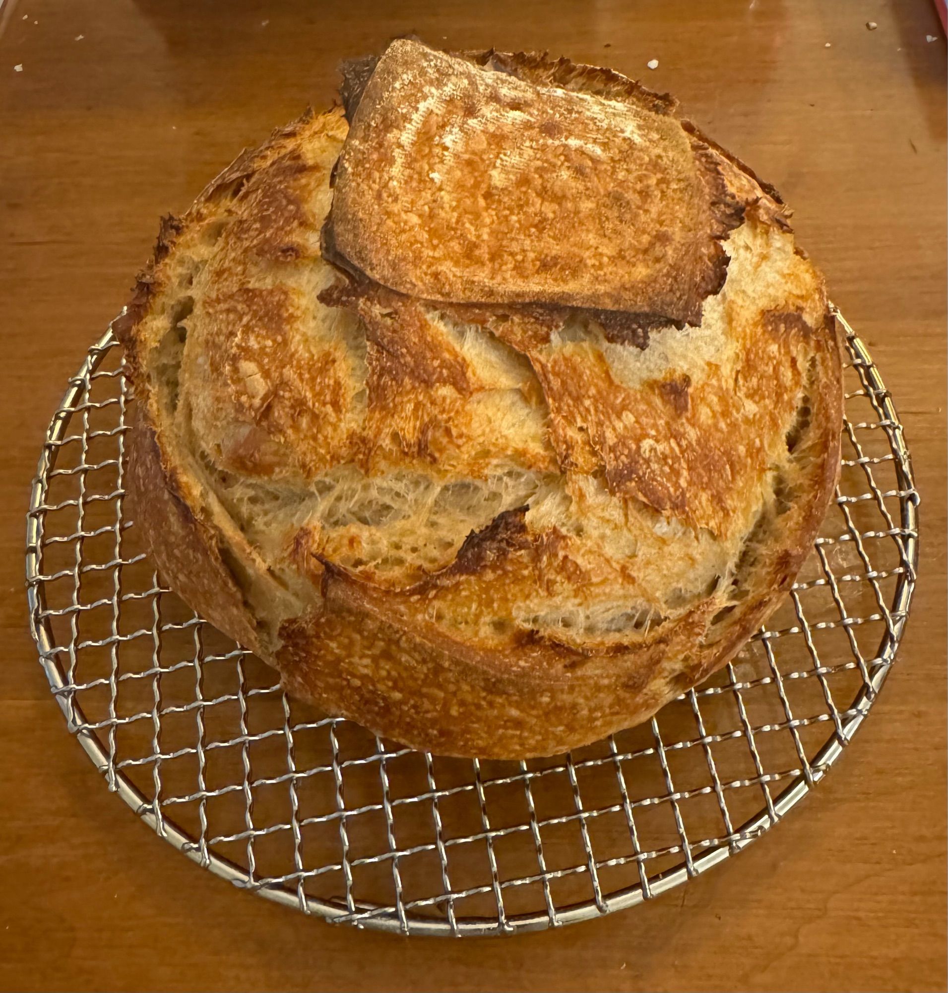 Sourdough boule on a round metal cooling rack on a wood table.