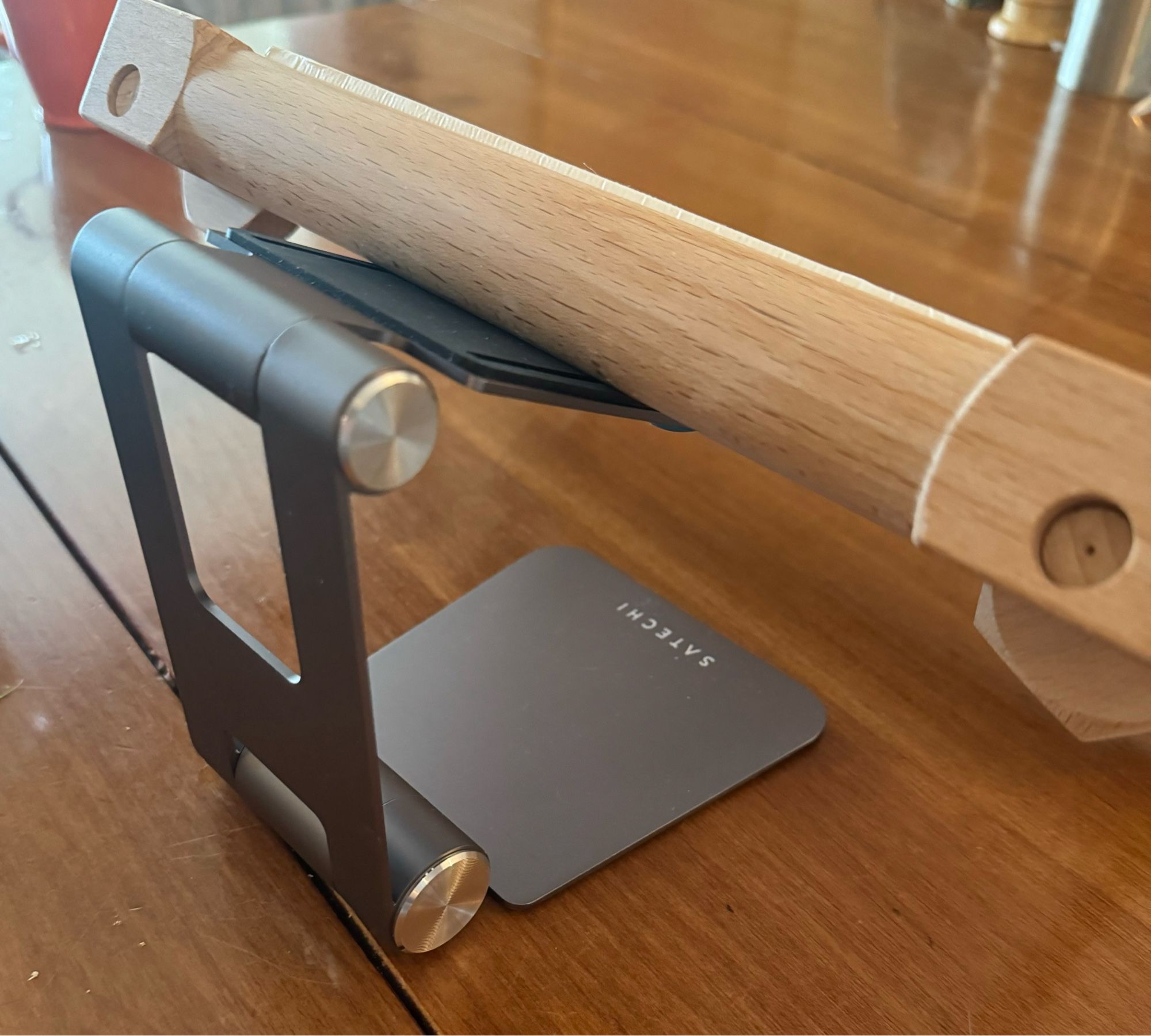 A wood scroll rod for embroidery is on a folding tablet stand on a wood table.