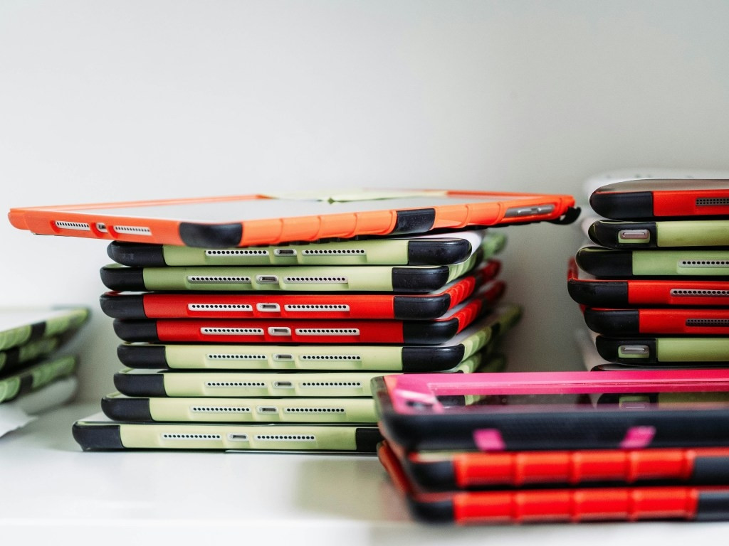 Image of several stacks of tablet computers in brightly coloured plastic cases