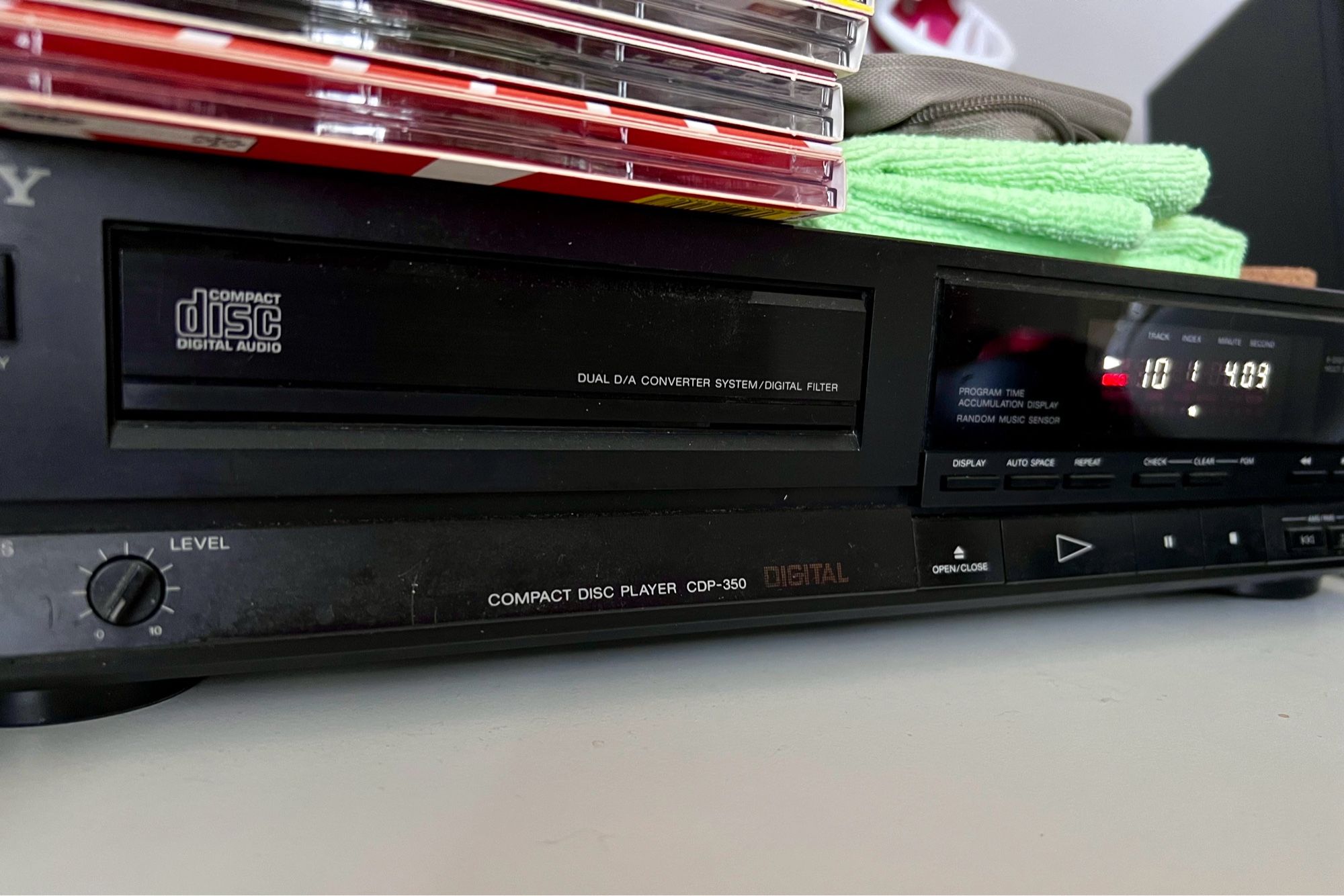 low semi-oblique view of a full-size black Sony CD player with a stack of CDs and a green microfibre cloth on top