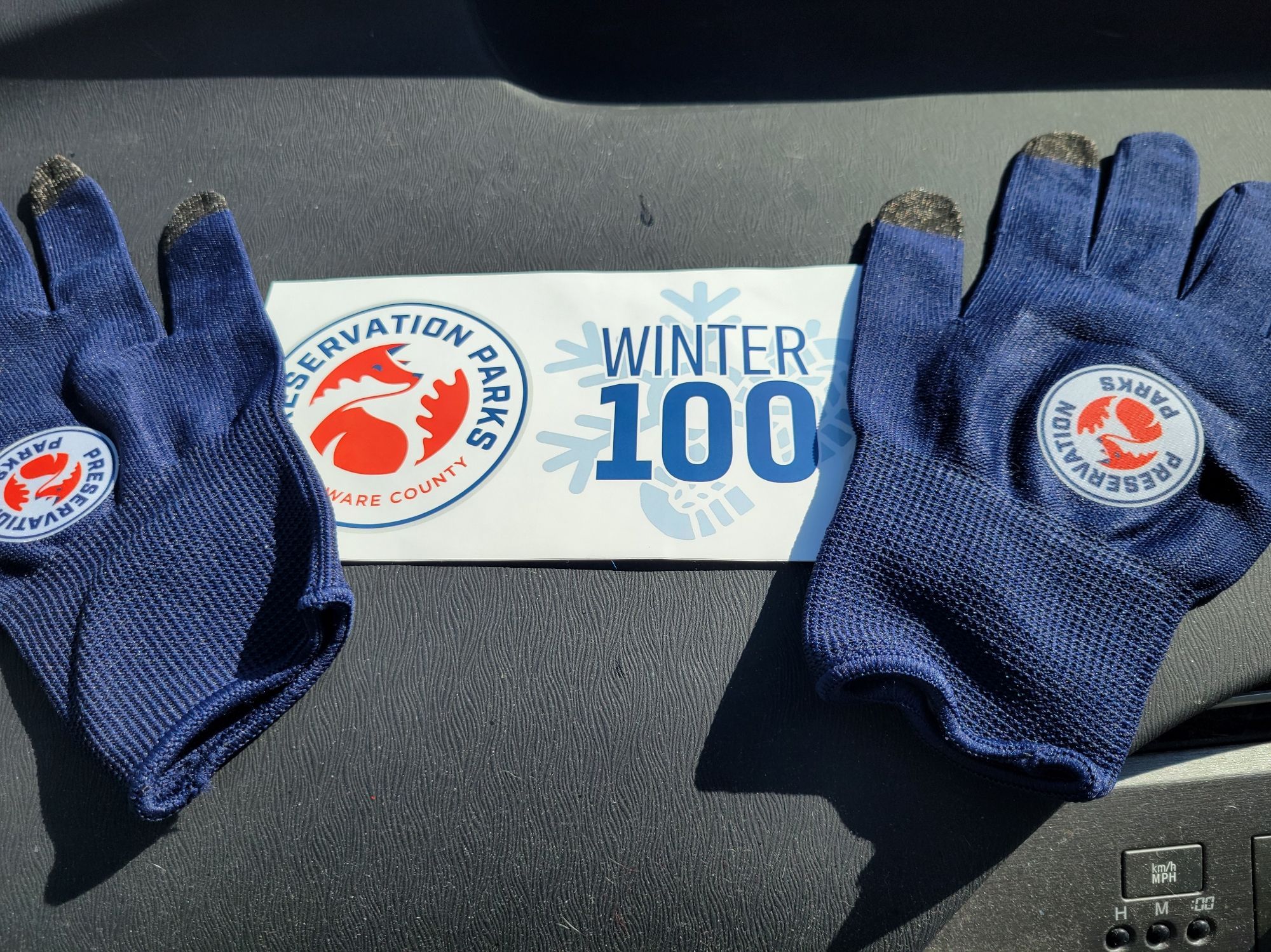 White bumper sticker and navy gloves with the logo "Winter 100."