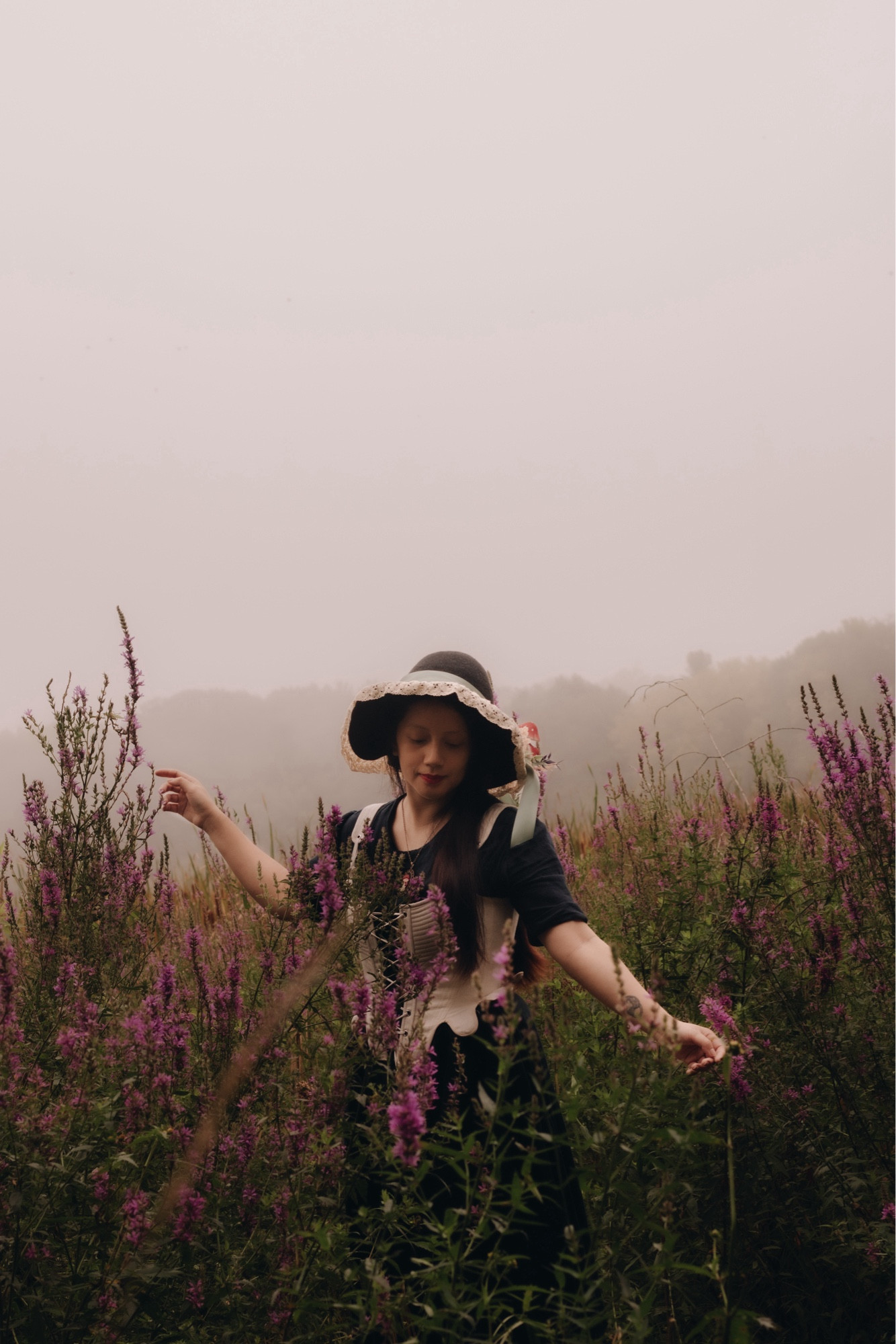 A girl, wearing a witch hat, surrounded by purple loosestrifes and fog.