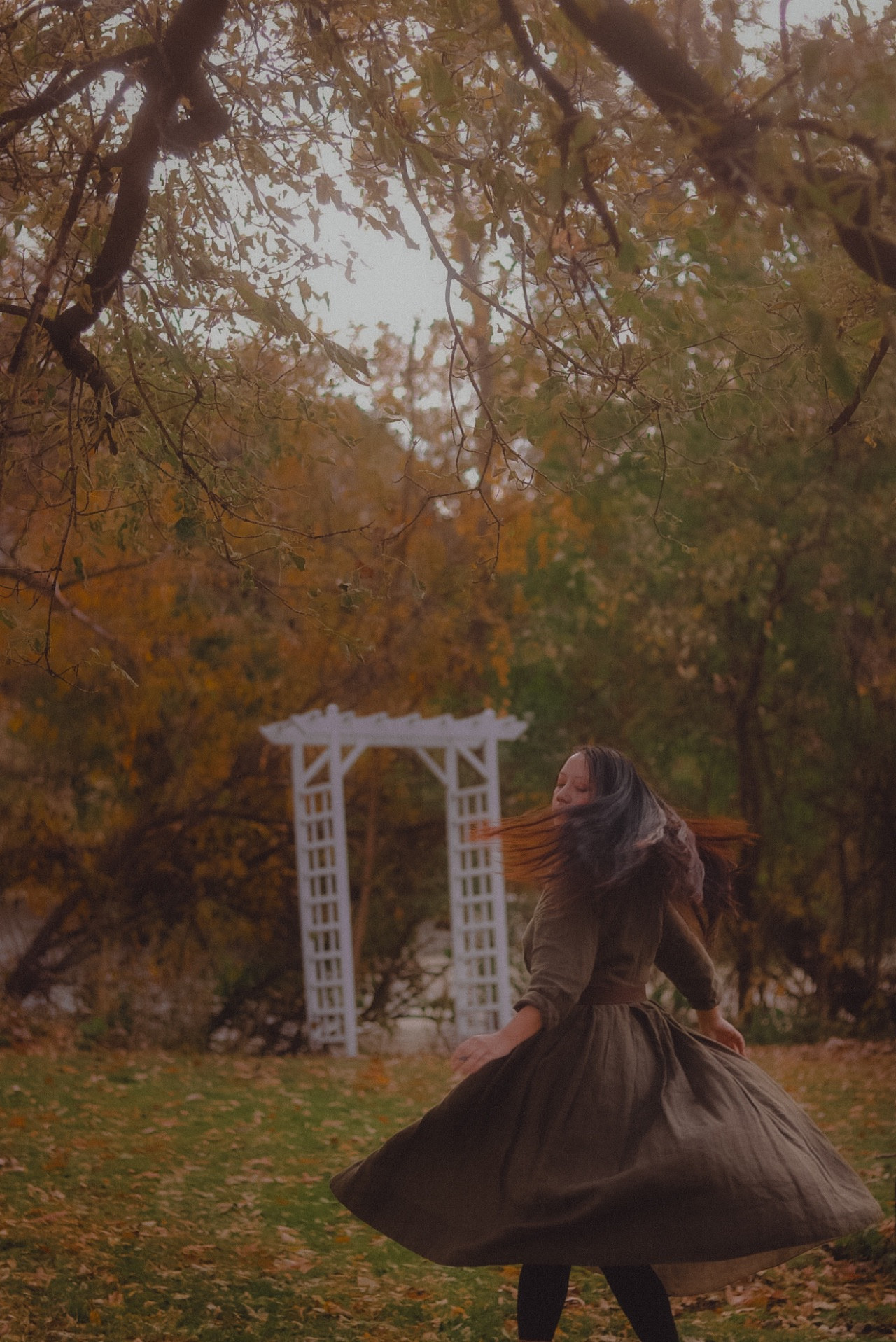 A girl, twirling in her dress, surrounded by fall foliage and fallen leaves.