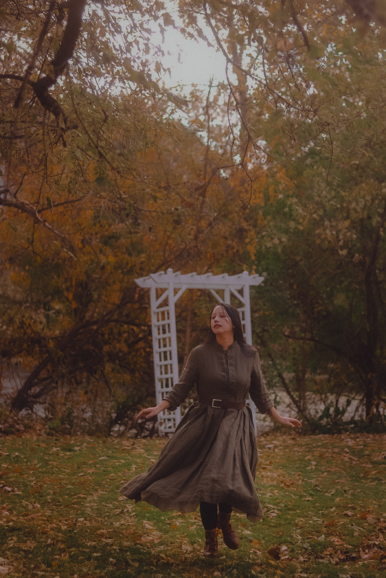 A girl, dancing in her dress, surrounded by fall foliage and fallen leaves.