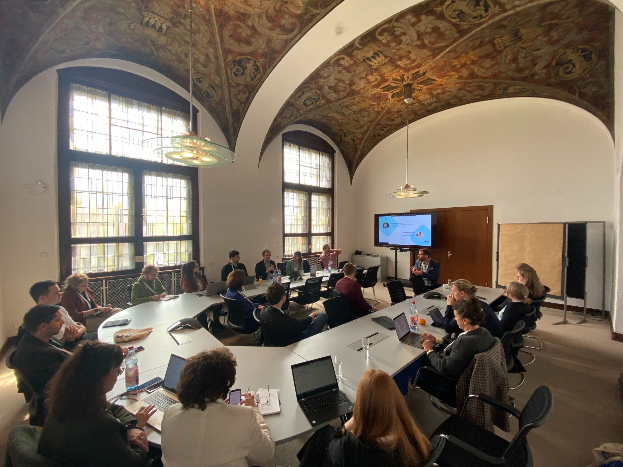 Präsentationsrunde beim UrbanDataSummit in Leipzig: Zu sehen sind ca. 20 Menschen an einem U-förmigen Konferenztisch, im Hintergrund die Präsentation. Foto: DKSR