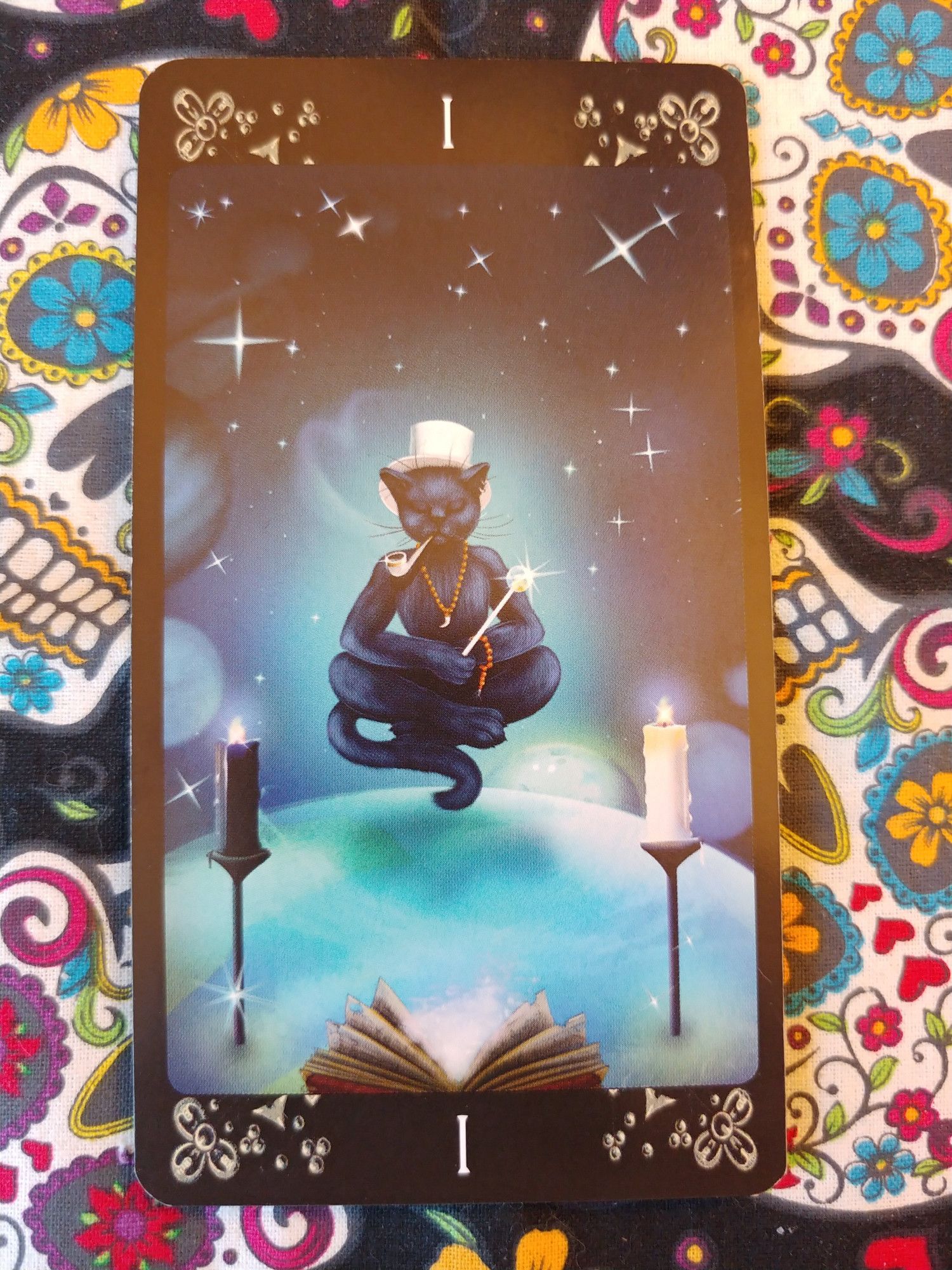 Card from the Black Cats Tarot deck.
The Magician-I.
A black cat sitting in a lotus pose meditating and levitating. He has a wand, a pipe in mouth. Two candles, a white and black, at his sides, and open book in front of him.