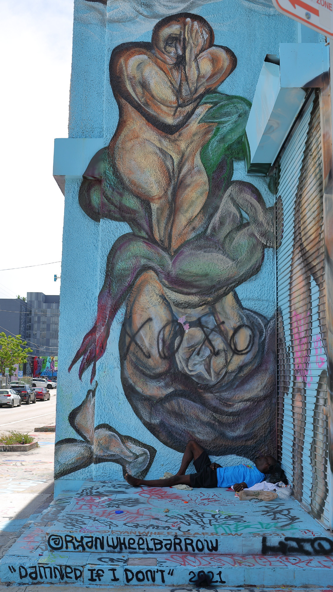 Homeless man sleeping in front of mural in Wynwood, Miami.