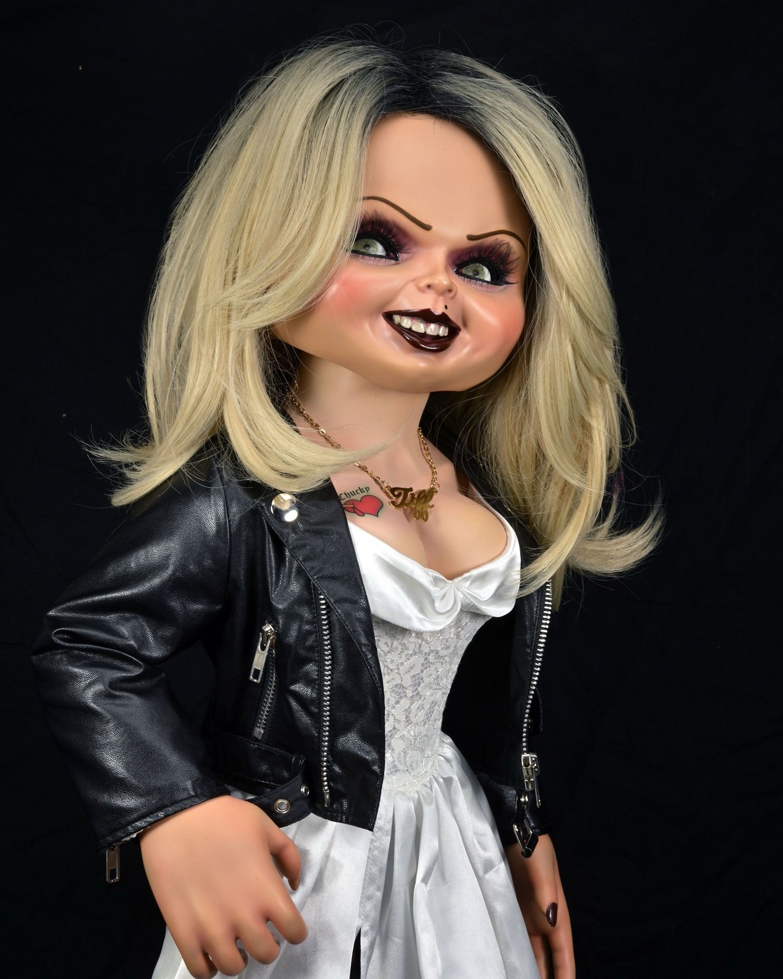 Tiffany, a child’s doll with shoulder length blonde hair, black lipstick, black eyeliner, a white dress that shows off her cleavage, a leather jacket, and a tattoo above her right breast.